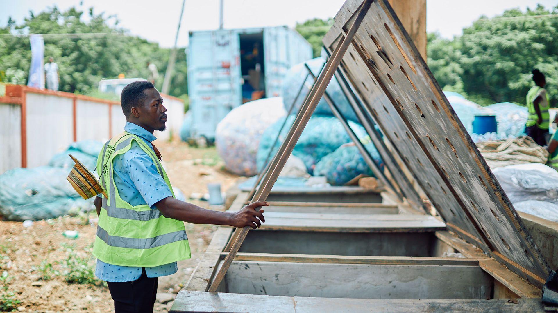 A man standing in a high vis jacket at a wooden waste facility with bags on plastic in the background. 