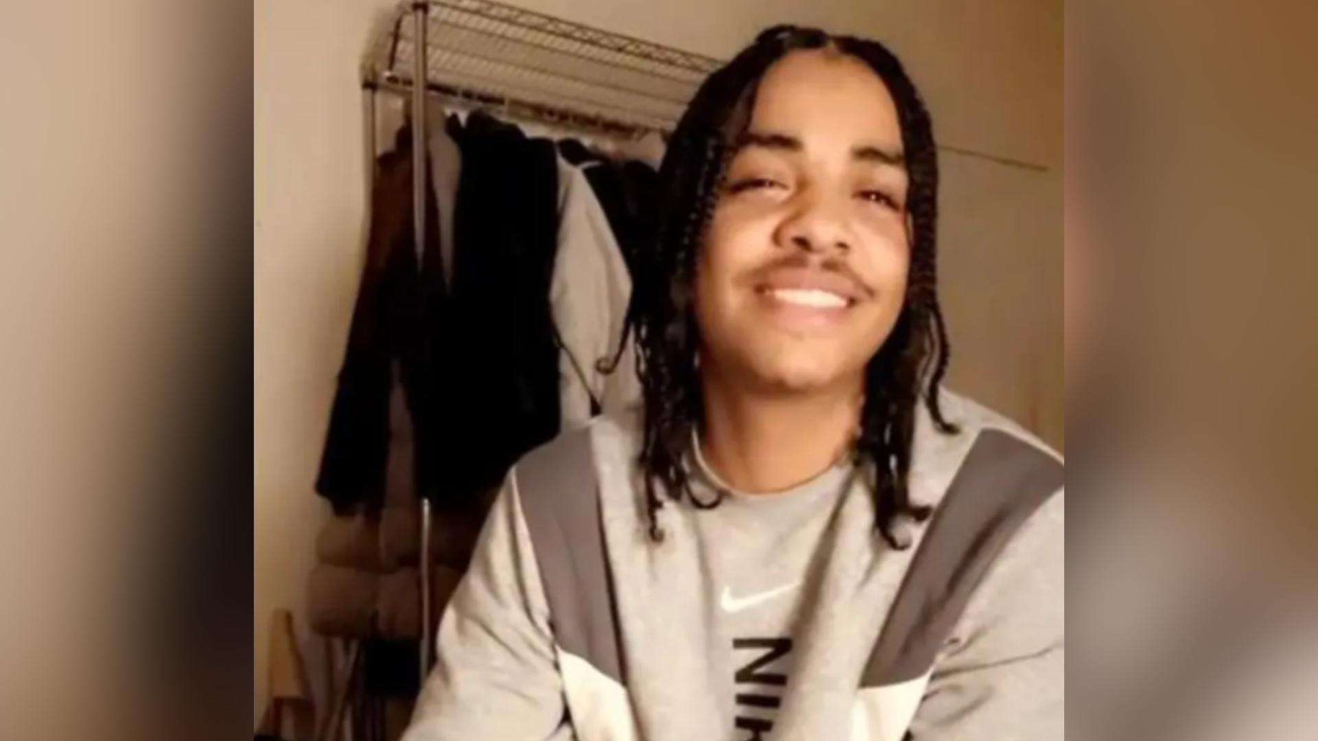 A man with tanned skin and hair in dreads looking at the camera and smiling. He is wearing a grey sweatshirt.