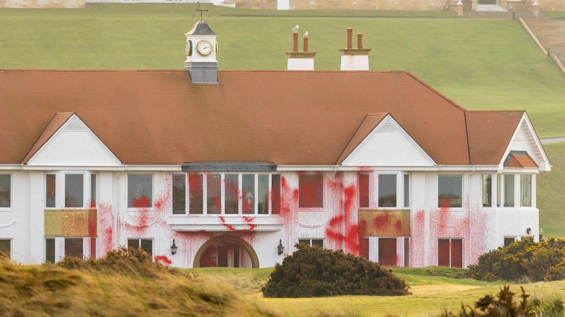 Red paint is daubed across a white building with red tiled roof. It is across the white stonework and windows. The main Turnberry hotel can be seen in the background.