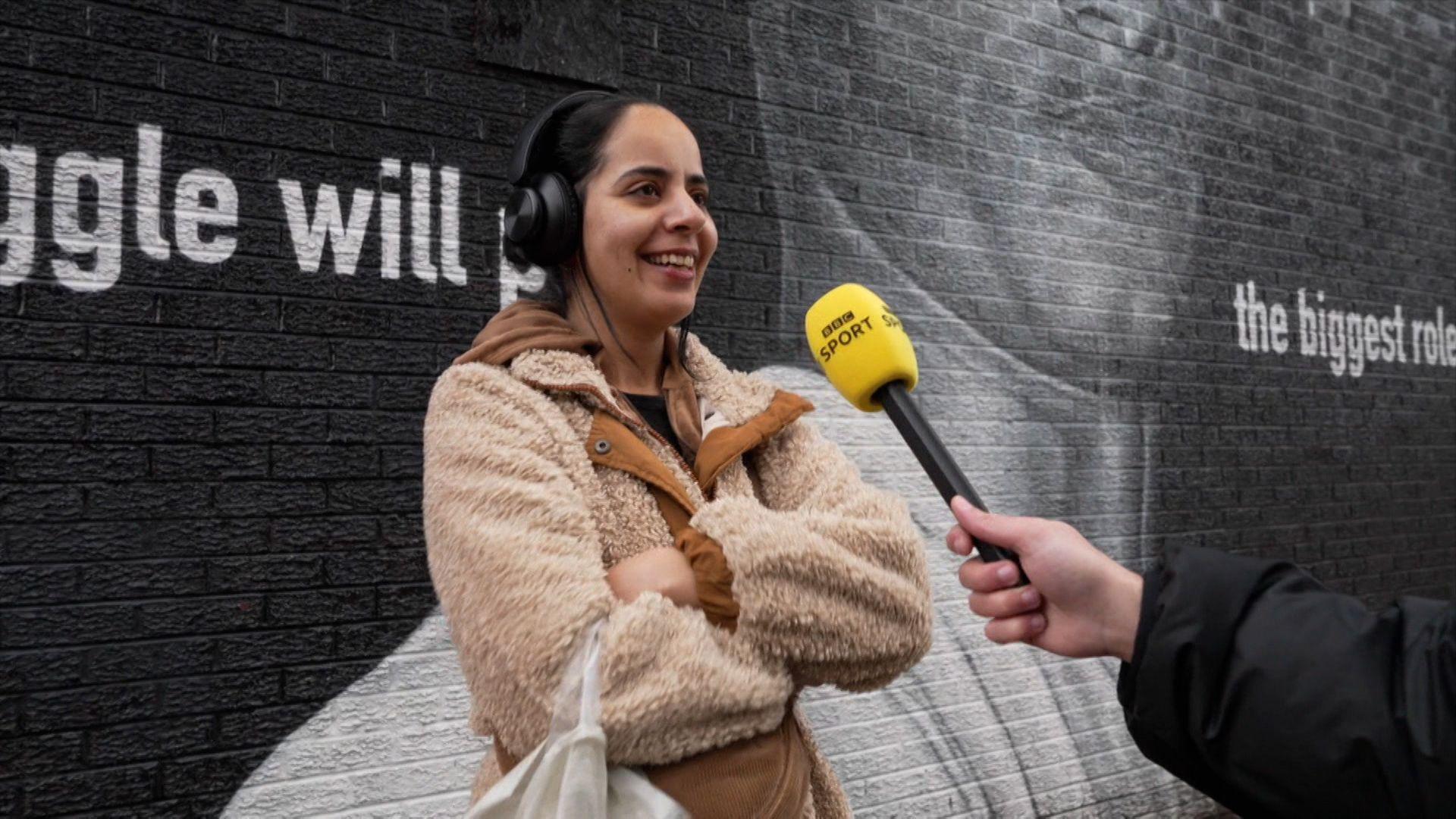  Manchester United fan Nusaybah Rwifa stands talking to a BBC reporter in front of a Marcus Rashford mural