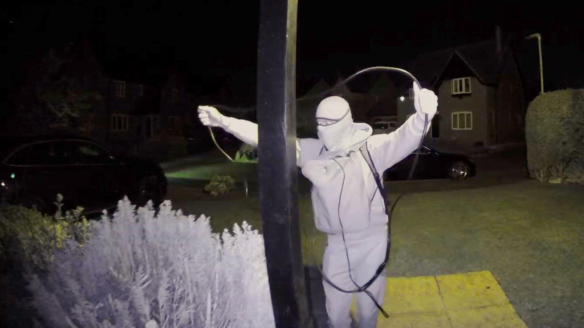 Man wearing a balaclava holding up a relay device while stealing a keyless car.