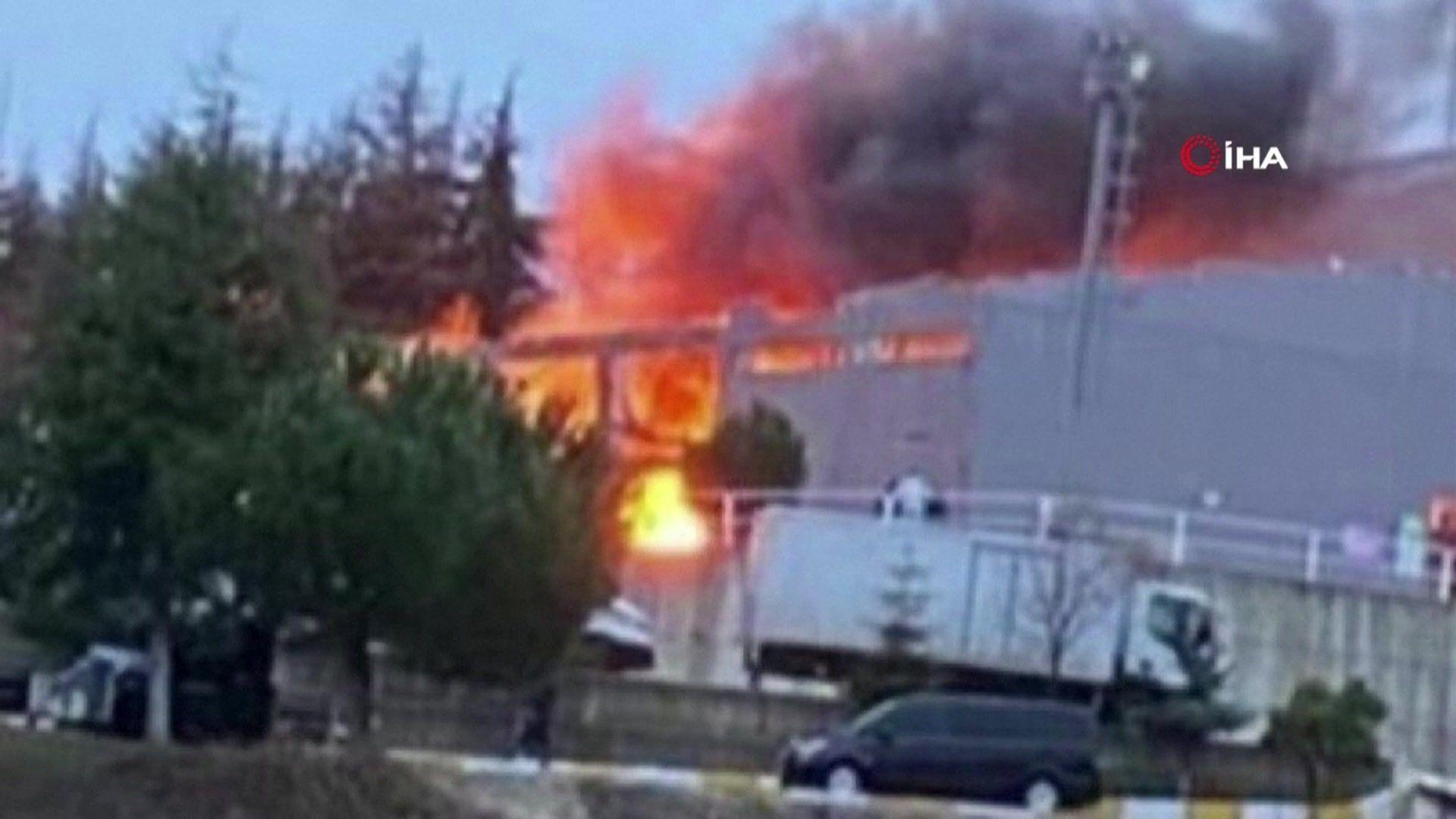 Part of an industrial building glows red as a fire engulfs the far side of it.