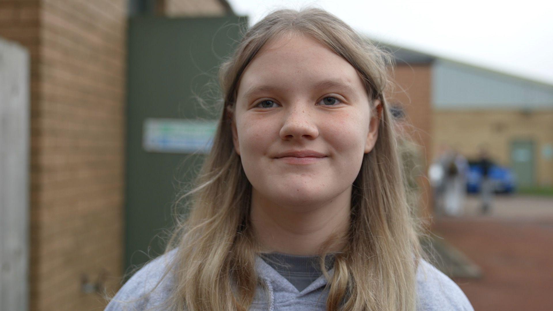 Cadet Cpl Taylor Knight, standing outside the cadet base in Cramlington in Northumberland. The 17-year-old has blonde hair and is wearing a grey hooded top and smiling. 