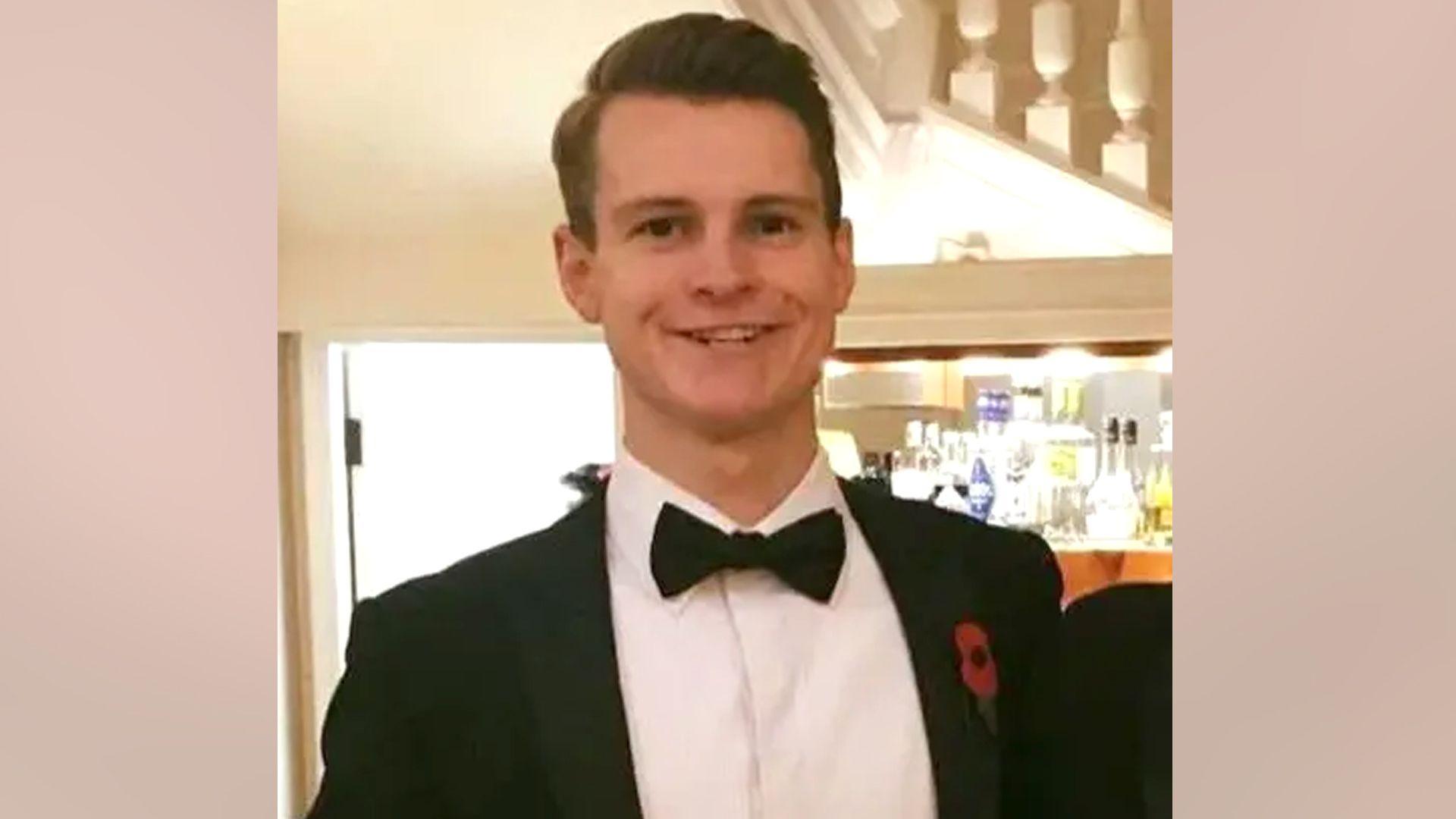 Alexander Cromie smiles in a tuxedo while holding a glass of wine.