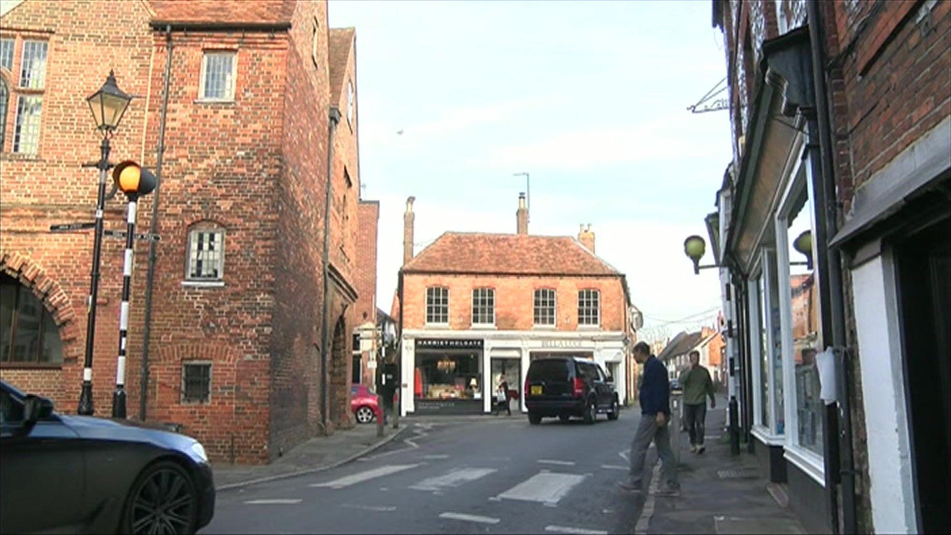 Watlington High Street. The road is narrow and there are tall red-brick buildings either side of the road.