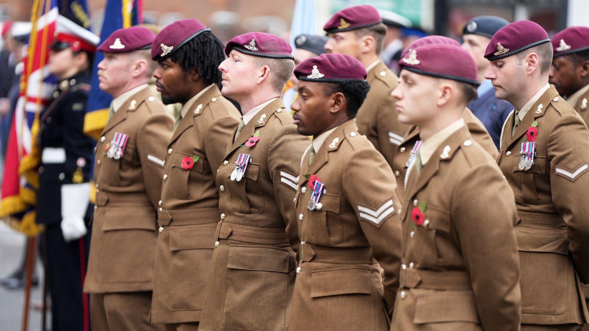 Soldiers stand in brown uniforms with crimson berets 