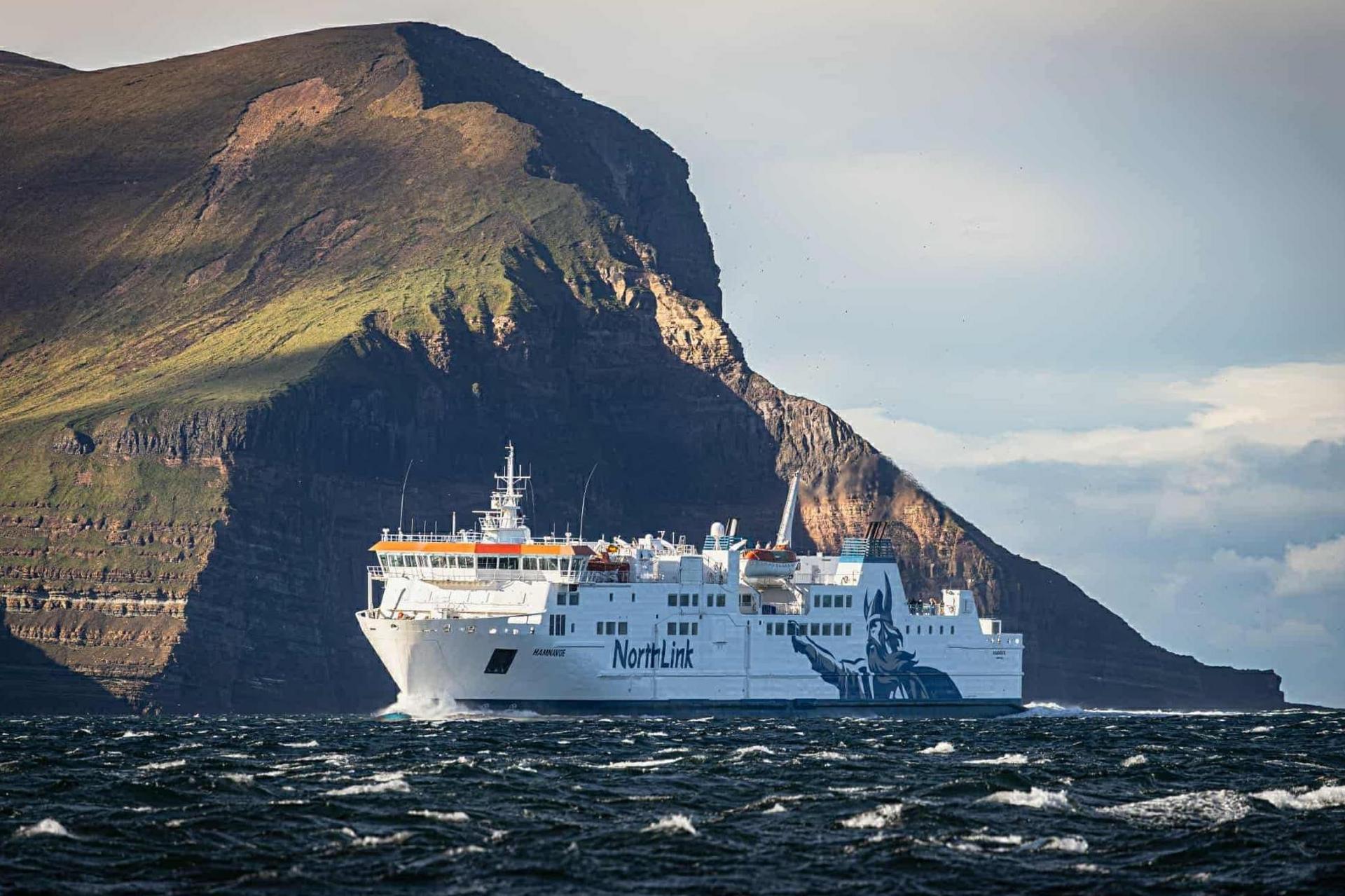 A large white ferry passes a high rocky headland.