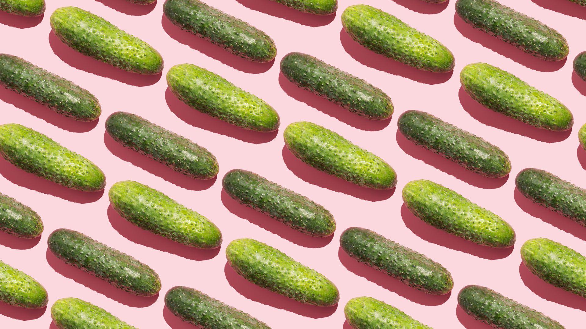 Pickles (gherkins) laid out in diagonal rows on a pale pink background.