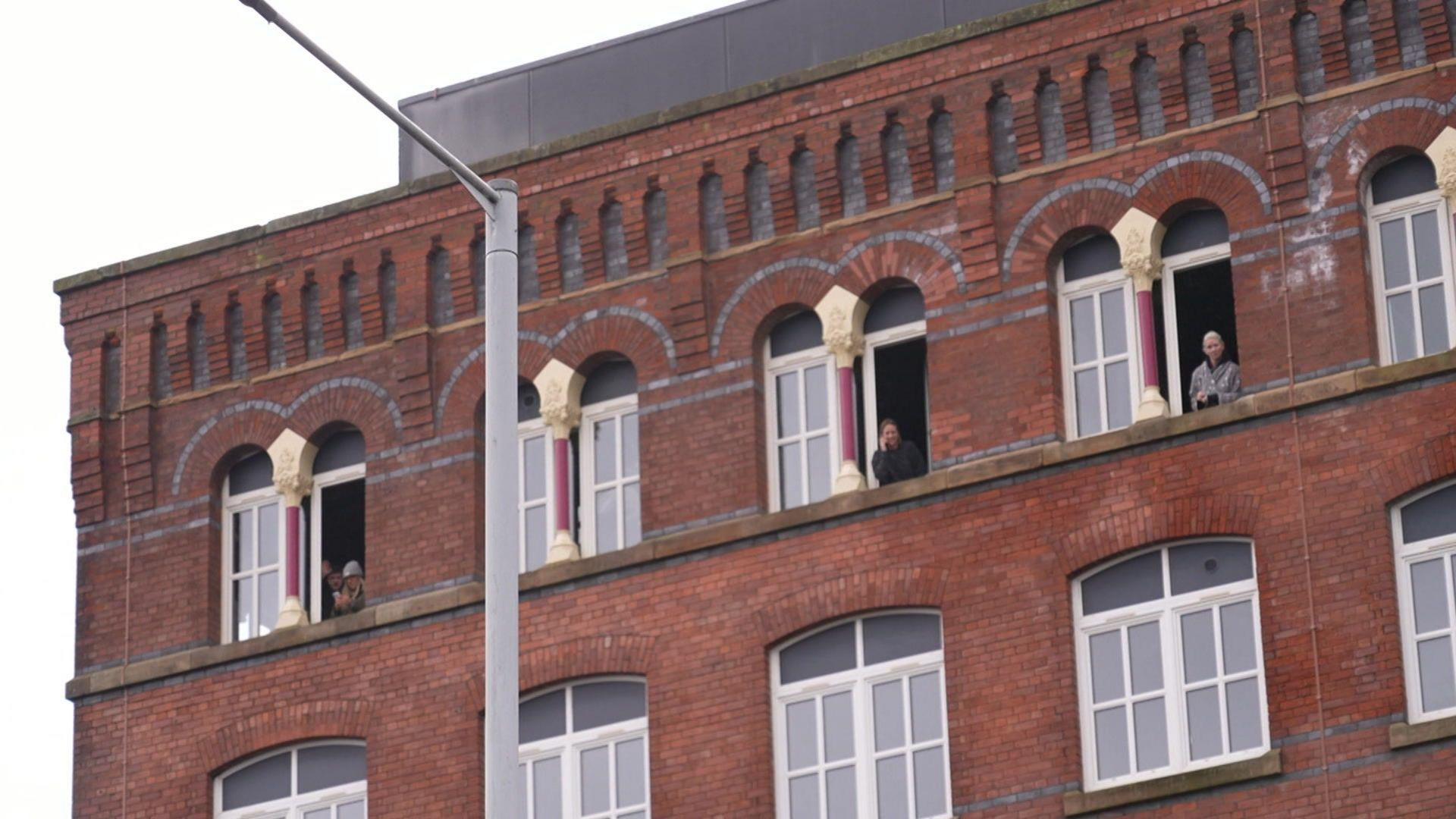 Three women look out of top-floor windows in a block of flats