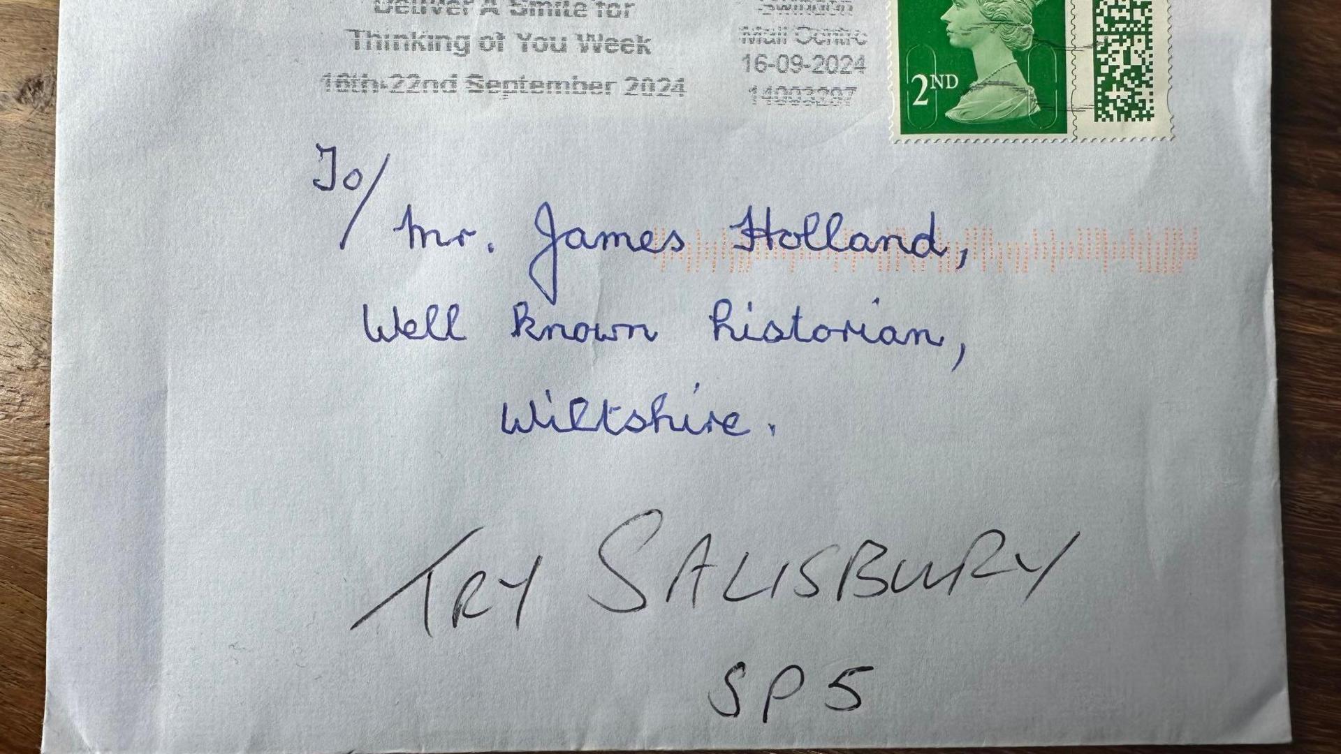 A white envelope with a second-class stamp addressed, handwritten in blue ink, to Mr James Holland, well-known historian, Wiltshire, with the words try Salisbury SP5 added in black ink underneath.