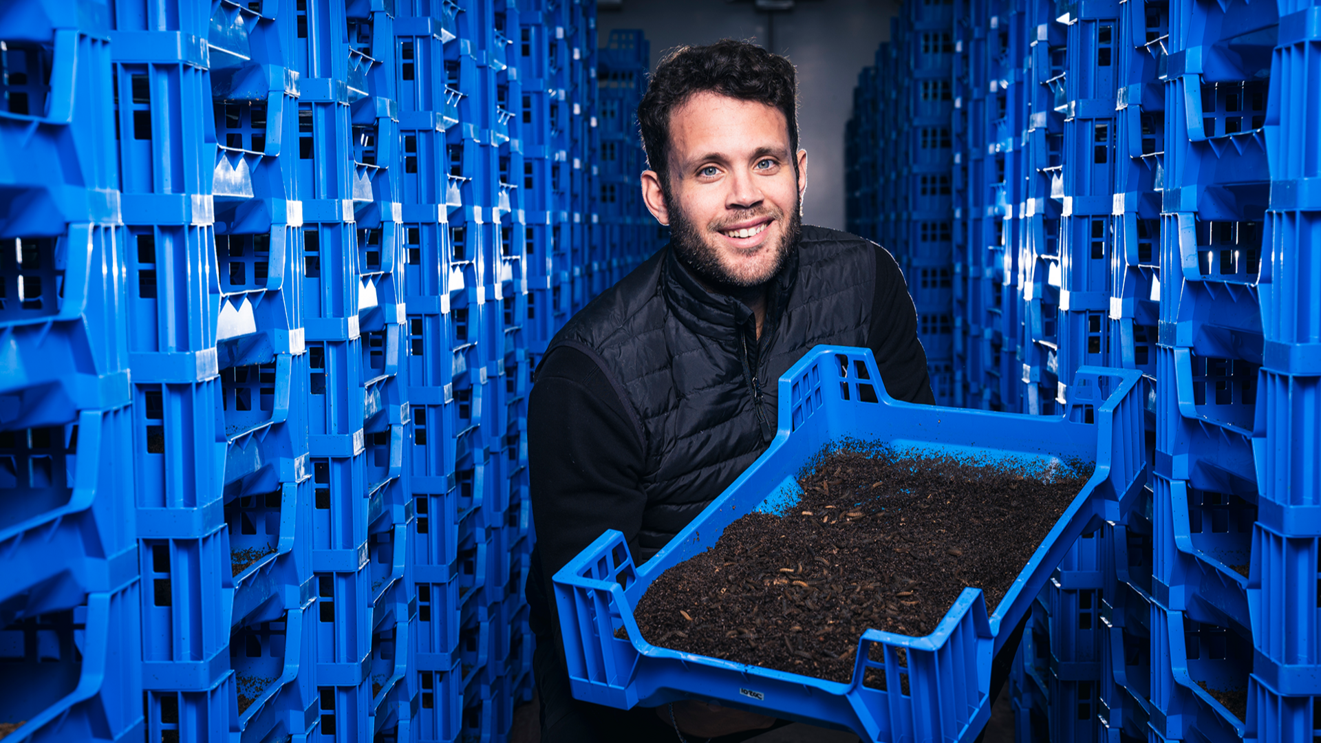 Larry Kotch holds a blue container full of fly larvae