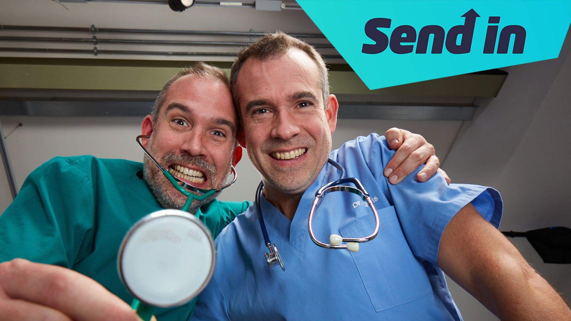 Dr Xand is holding a stethoscope the camera and has his arm around Dr Chris who is wearing a stethoscope around his neck. They are both wearing scrubs and looking down into the camera