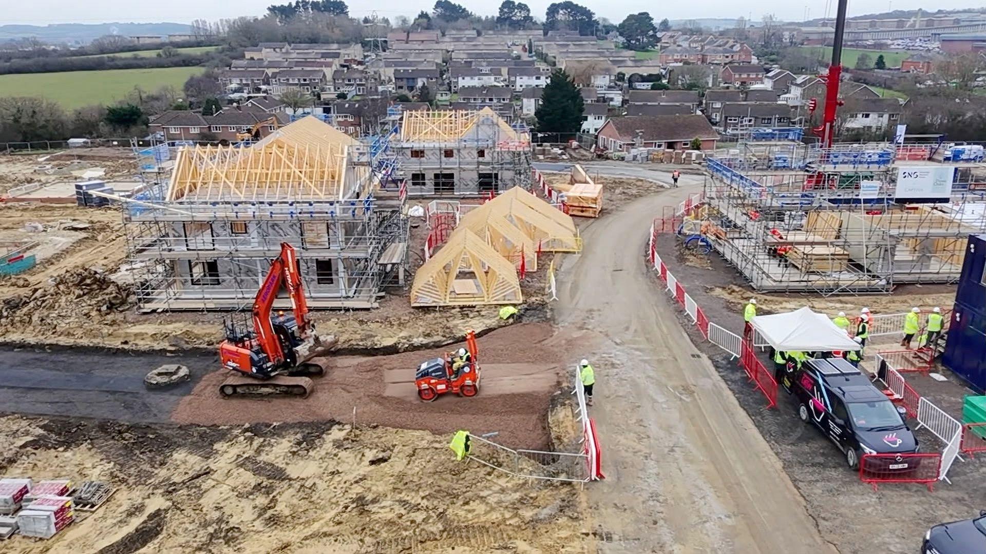 A construction site on the Isle of Wight. There is heavy machinery and half-finished constructions in the frame as well as men in high-vis jackets.