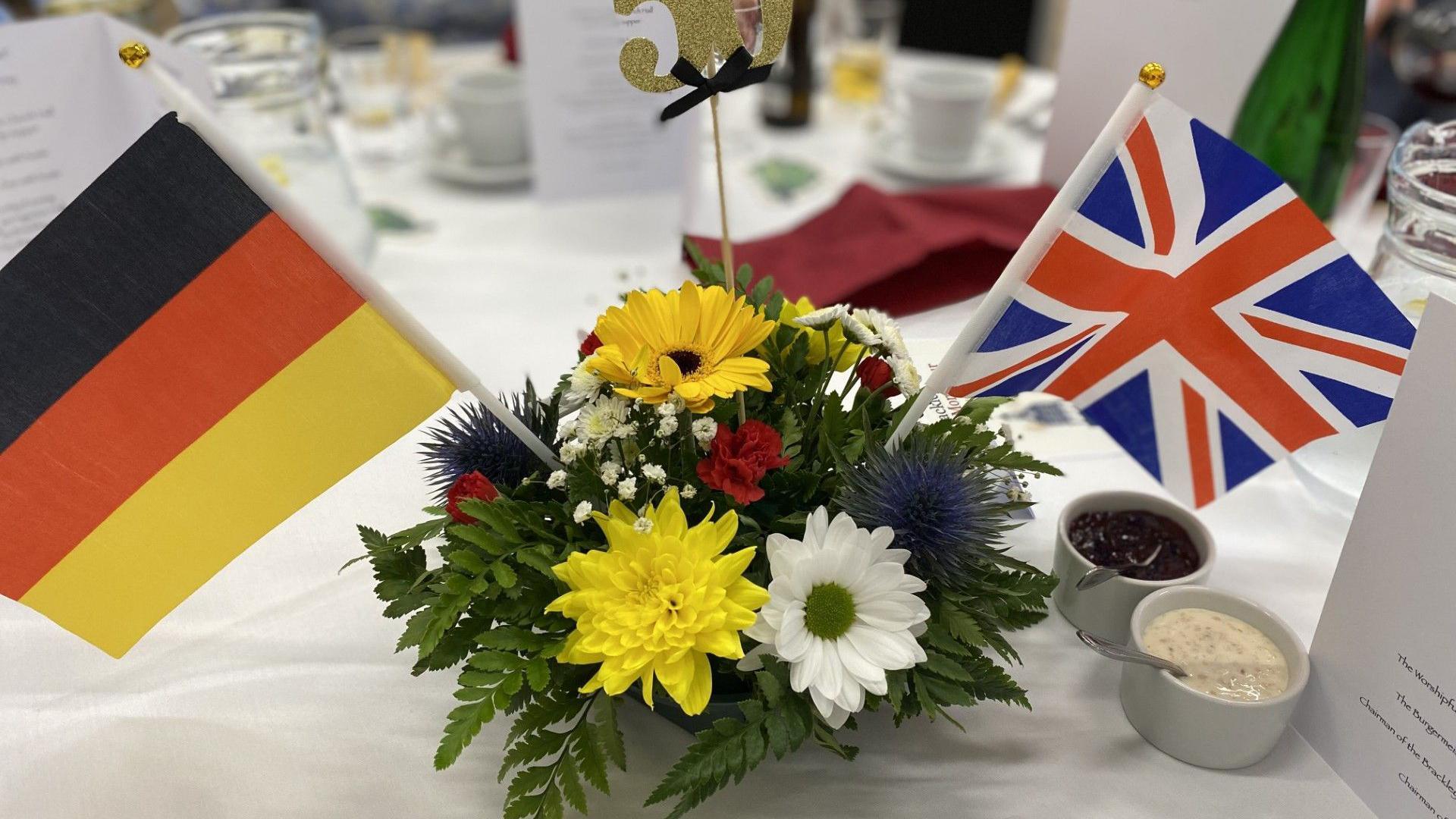 A decorative plant with the flags of Germany and the United Kingdom on a white table.