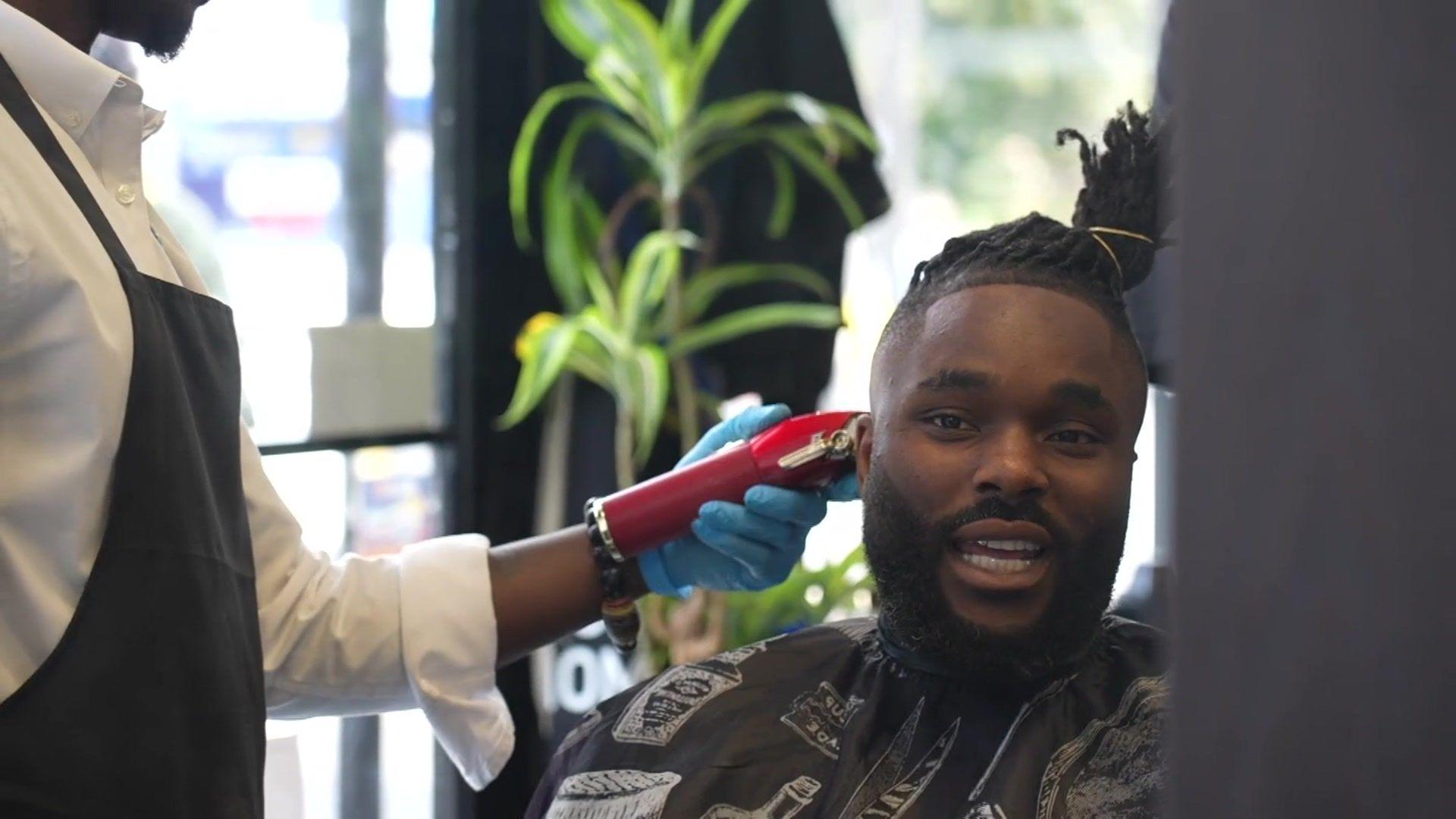 A staff member at Jul's barber shop in south London looks at a customer while testing his blood pressure with an out-of-shot machine that has a cuff