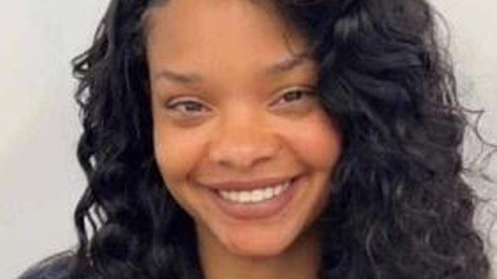 A smiling young woman with long curly dark hair and brown eyes. 