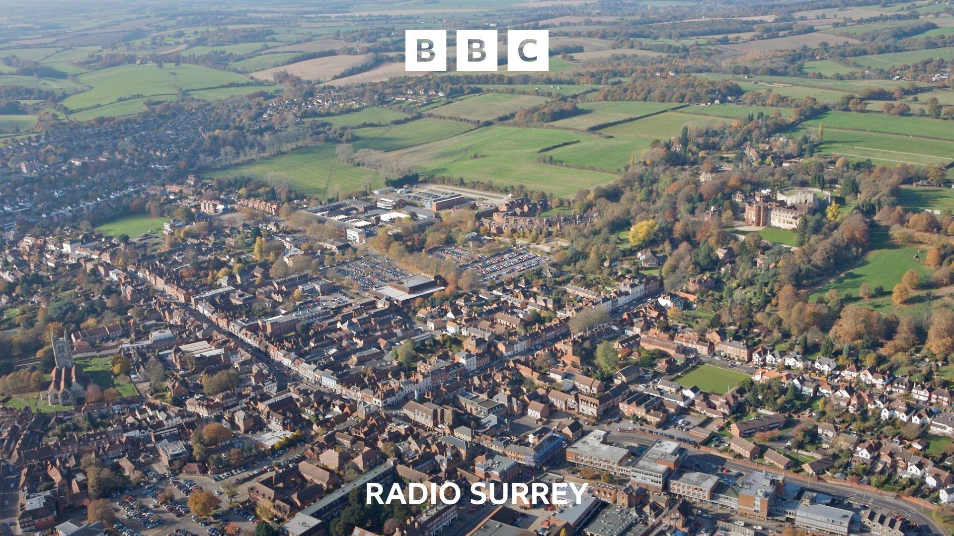 An aerial view of Farnham. Houses and commercial buildings fill the bottom half of the image. In the top half, fields and trees are visible stretching off into the horizon.