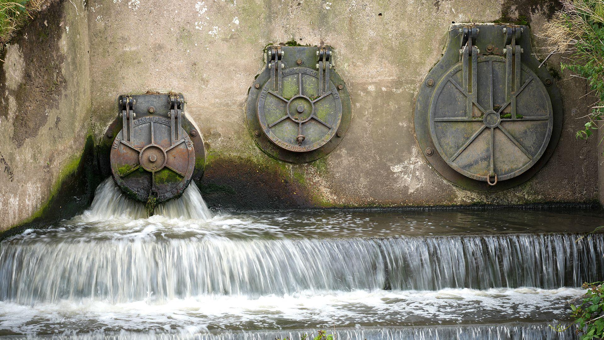 Water discharges from three cylindrical utlet pipes into the River Mersey next to the United Utilities waste water treatment plant in Stretford on June 23, 2025 in Manchester