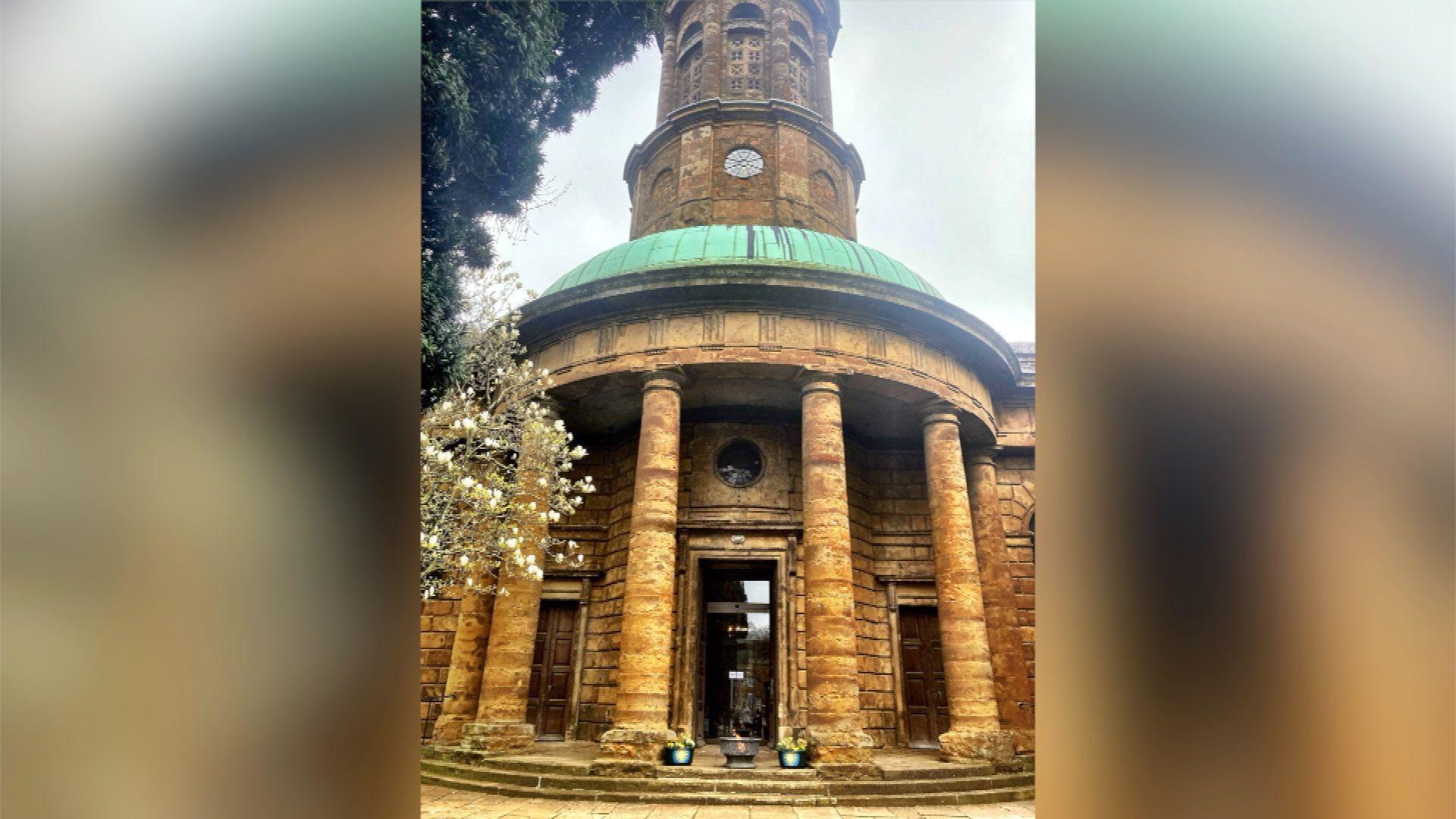 An exterior view of St Mary's Banbury, it is an old yellow brick building, with pillars and a turquoise round roof and a clock tower