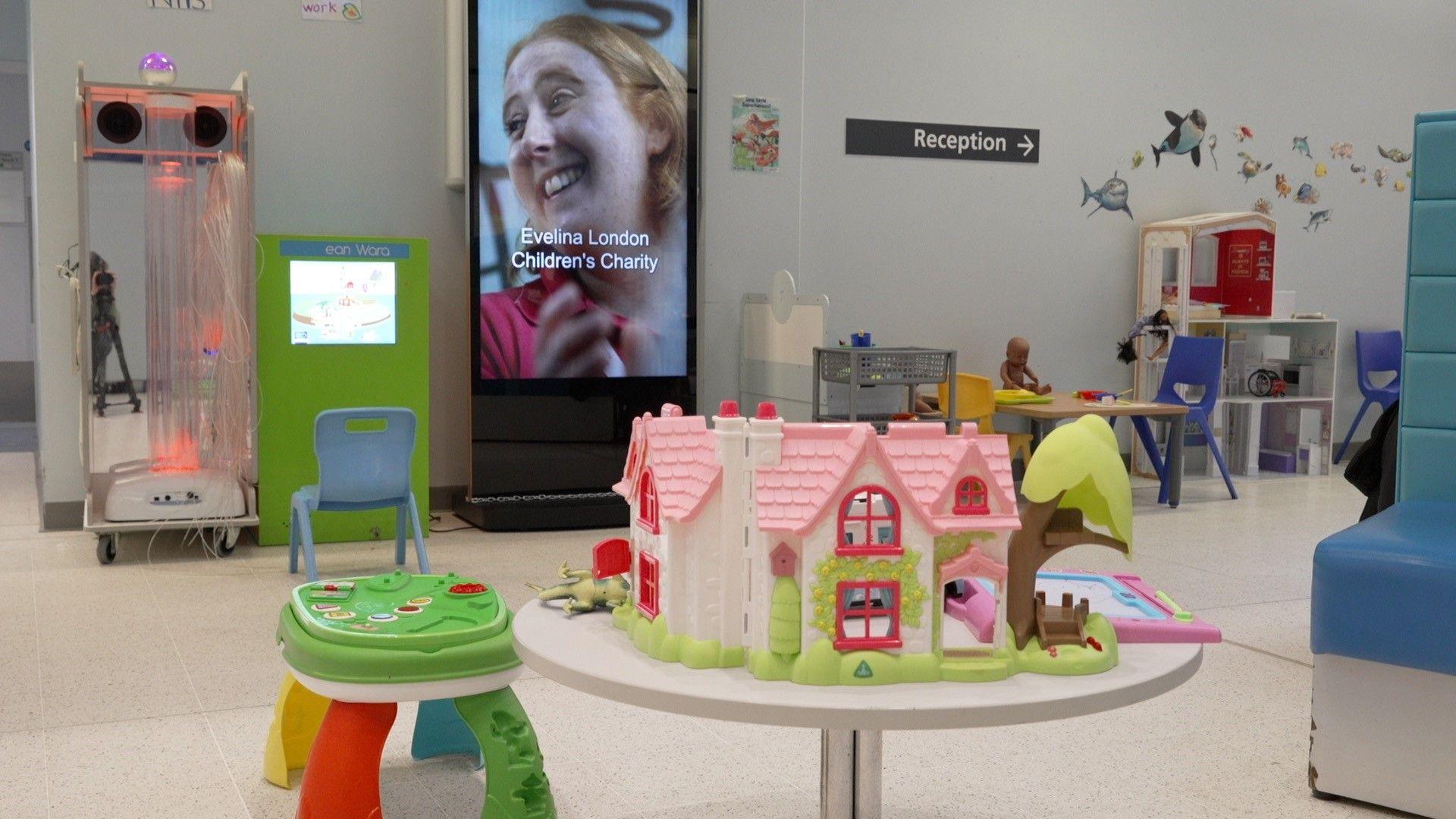 A waiting area in the hospital. There are toys around the edge of the room, and a plastic play house on a table. 