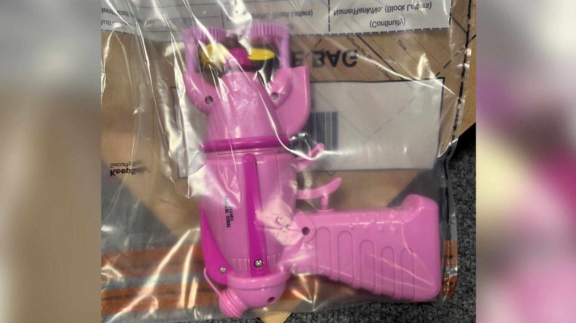 A pink, plastic toy bubble gun is seen concealed in a plastic bag.