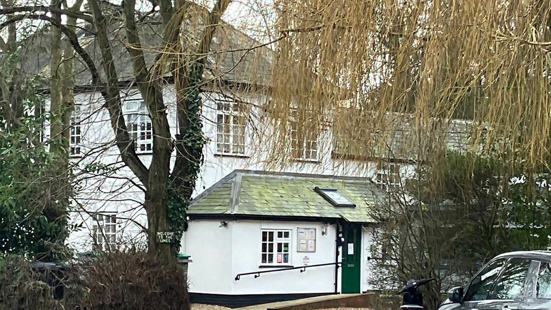 A view of the front of the care home - a white building - from the end of the driveway. 