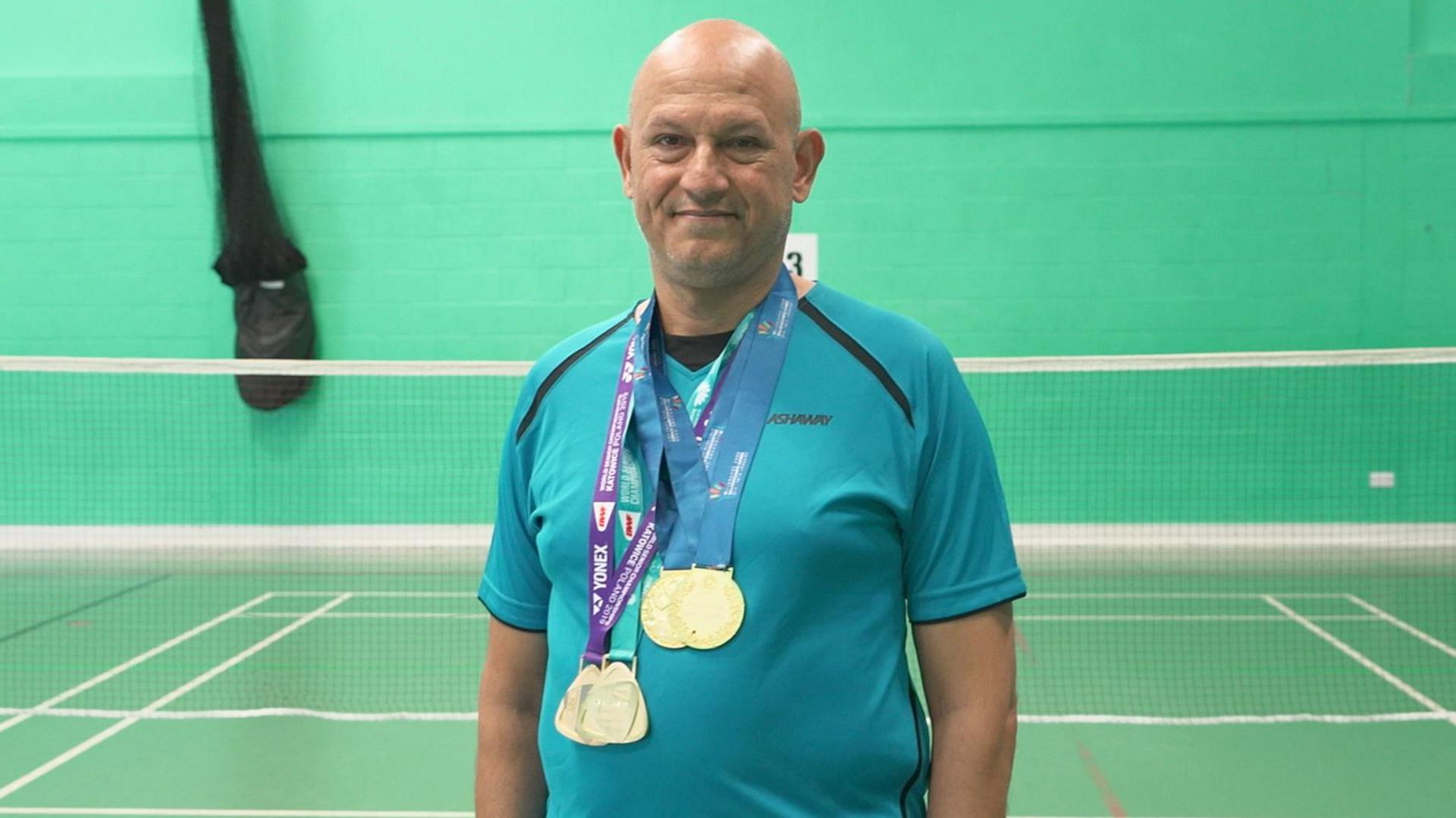 Rajeev is smiling looking directly at the camera. He is wearing his medals and is dressed in a blue t shirt