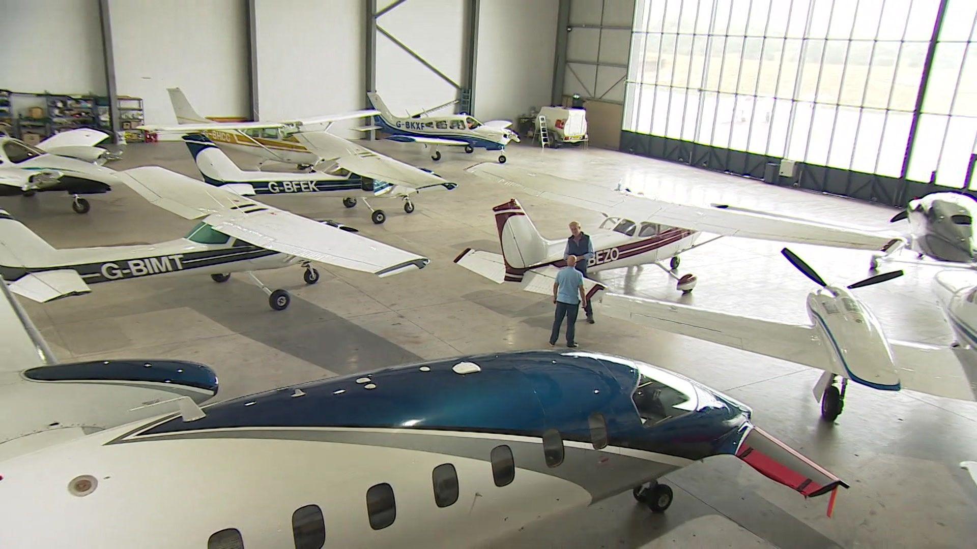 Two people in an airport hangar filled with small planes.