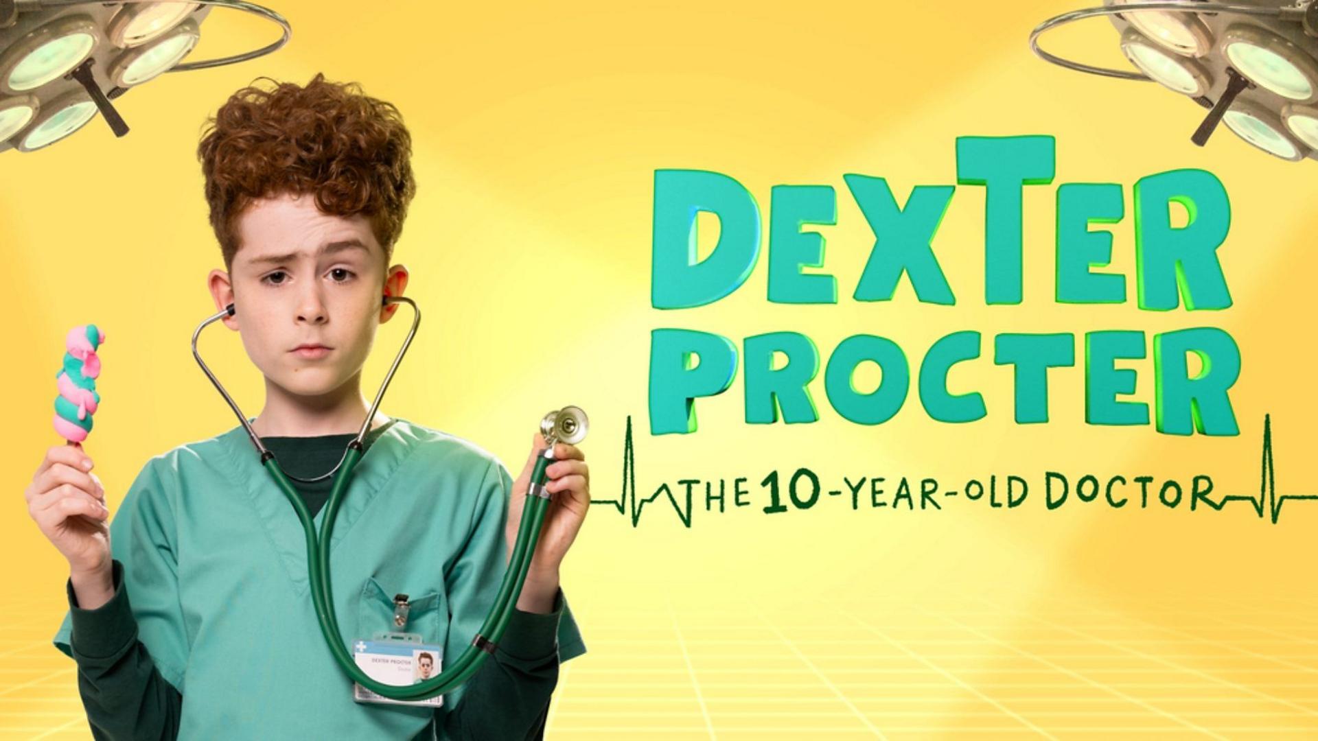A young boy stands to the left of the image in front of a yellow background. He is holding a pink and blue ice lolly in one hand and a stethoscope in the other. The stethoscope earpieces are in his ears. He has auburn curly hair piled on top of his head and he is wearing blue/green scrubs with a dark green long-sleeved top underneath. There are surgery lights in the corner of the image and on the right are the words Dexter Procter in the same colour as the scrubs and then the 10 year-old-doctor is written underneath in between heart monitor lines
