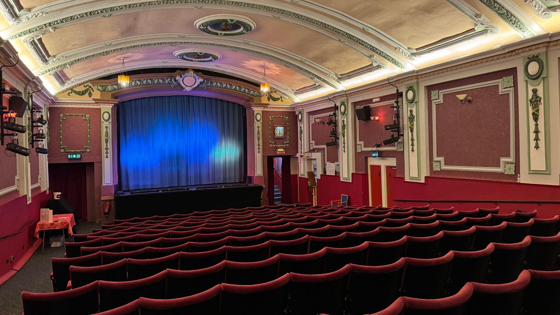 An empty cinema pictured from the back with red seats and a blue curtain in front of the screen.