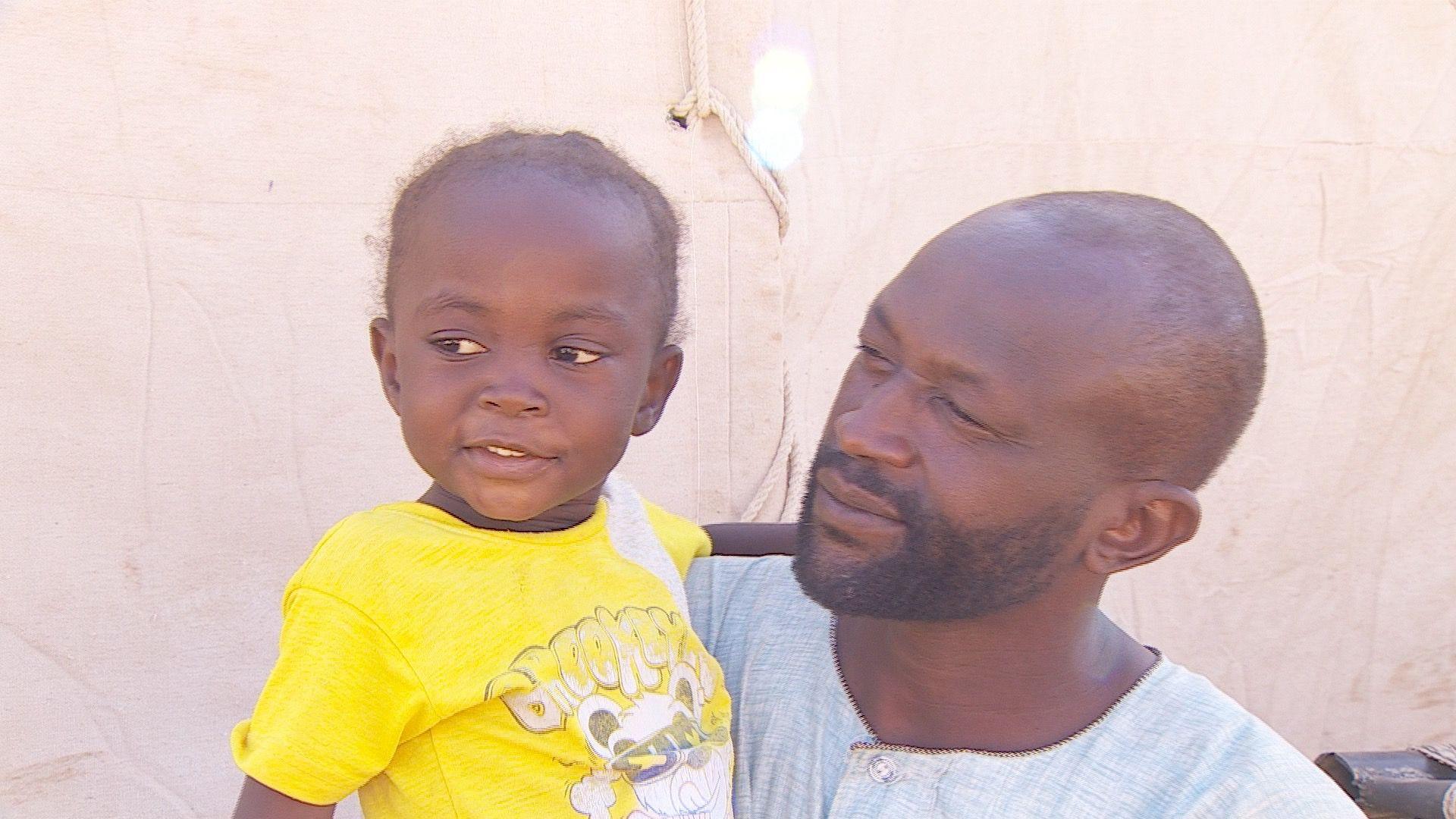 Abdullah Adam Mohamed, holding one of his young daughters who is wearing a yellow T-shirt