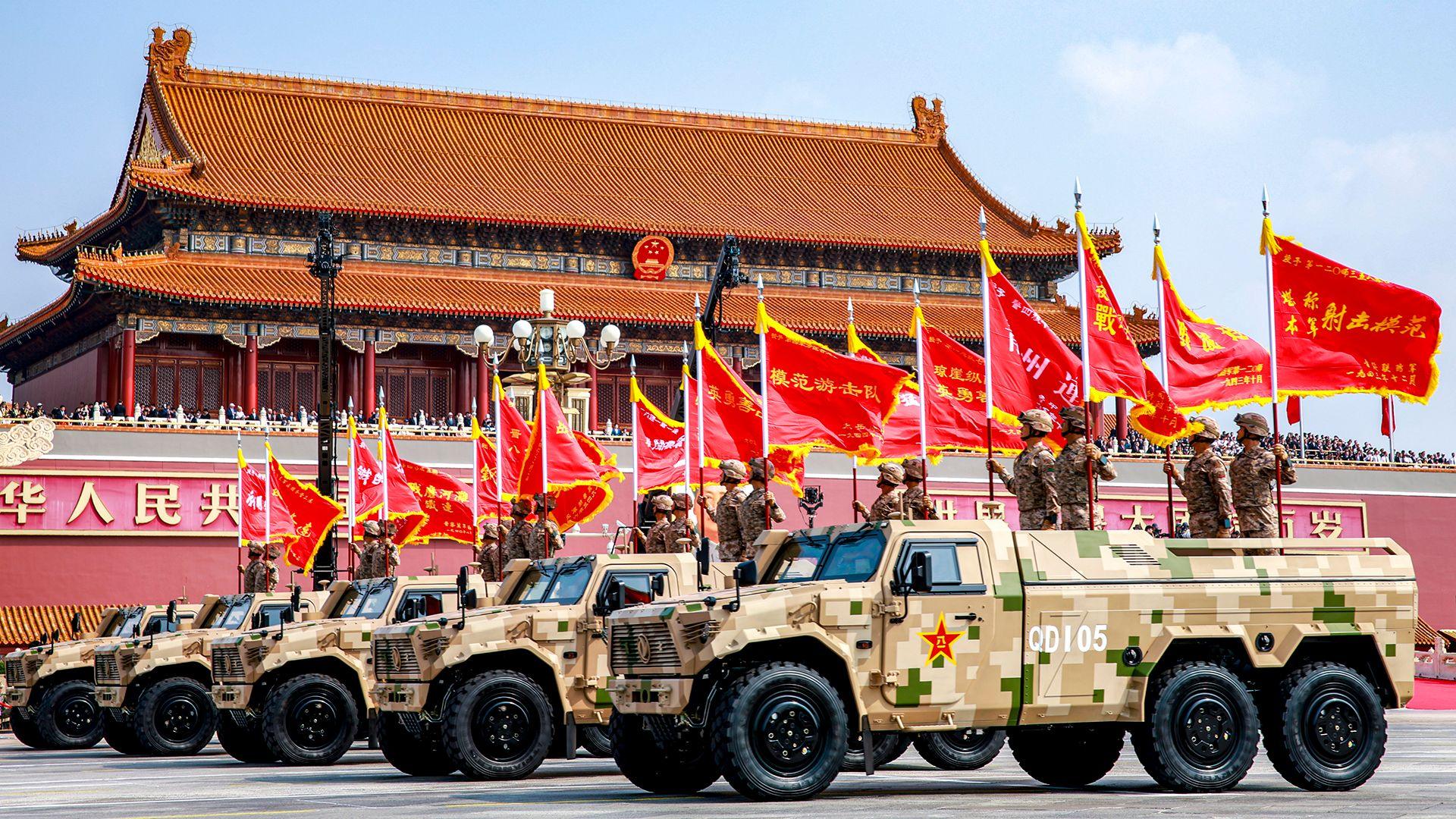 Military vehicles have soldiers on them carrying red flags on top as they parade through Tianeman Square on Wednesday.