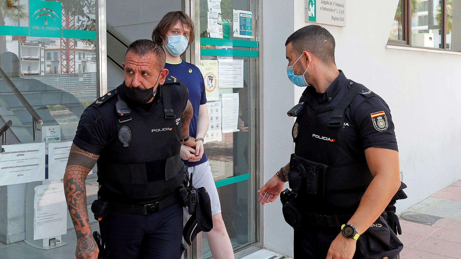 A man in handcuffs is escorted by two police officers out of a building.