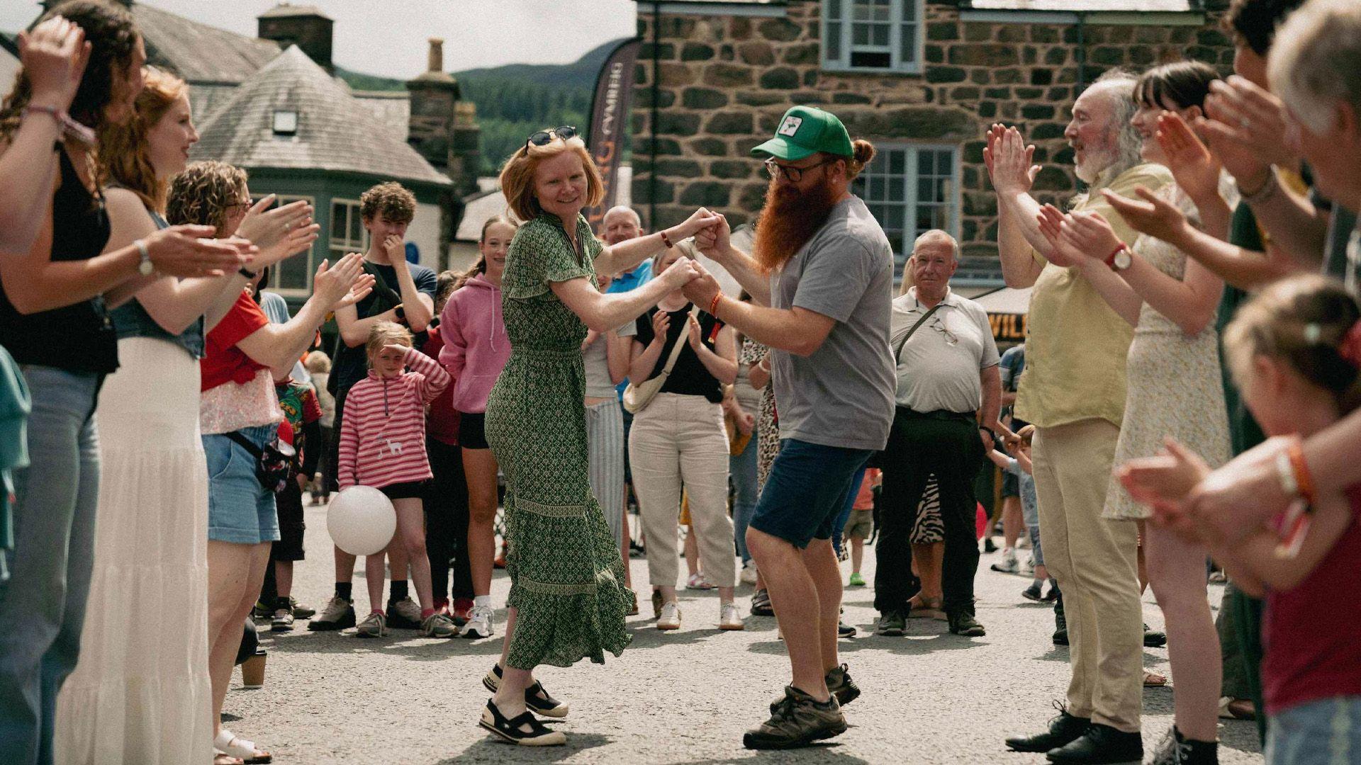Cwpl yn mwynhau twmpdaith ar sgwâr Dolgellau yn ystod y Sesiwn Fawr