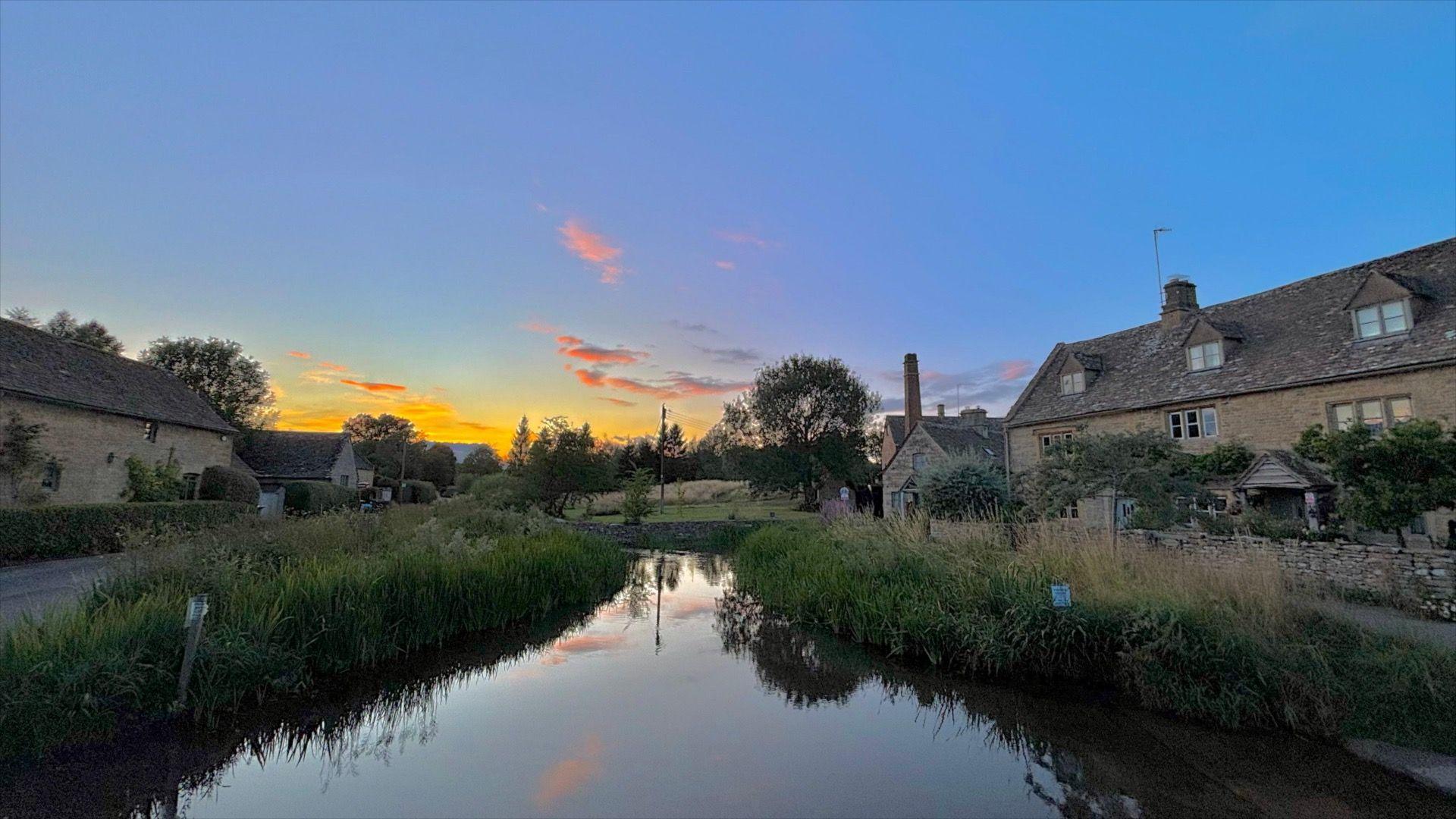 A yellow sky with Cotswold buildings on the side and a river in the middle. 