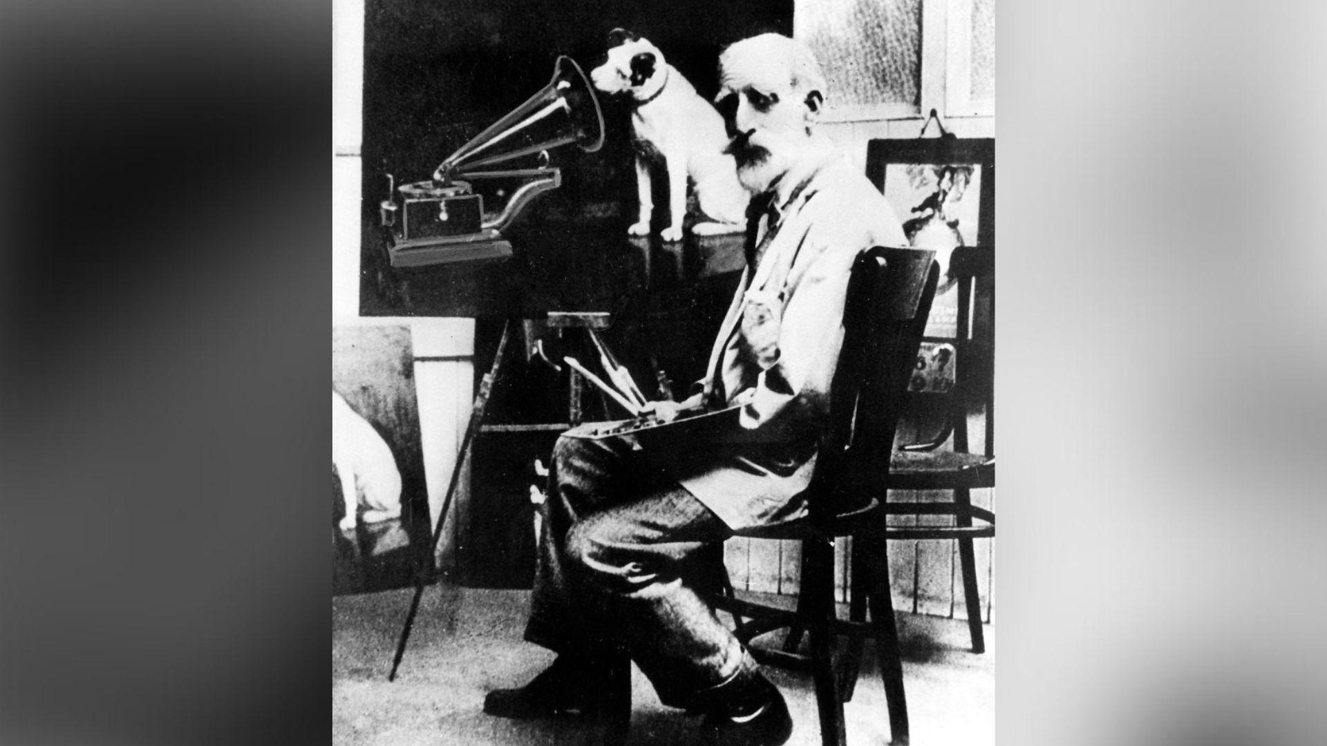 A black and white photography of a man, sitting on a chair. He is painting a dog listening to a gramophone.