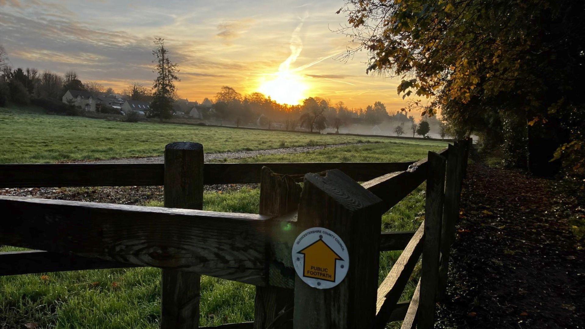 Sun setting with the mist and a field in front with trees and a fence.