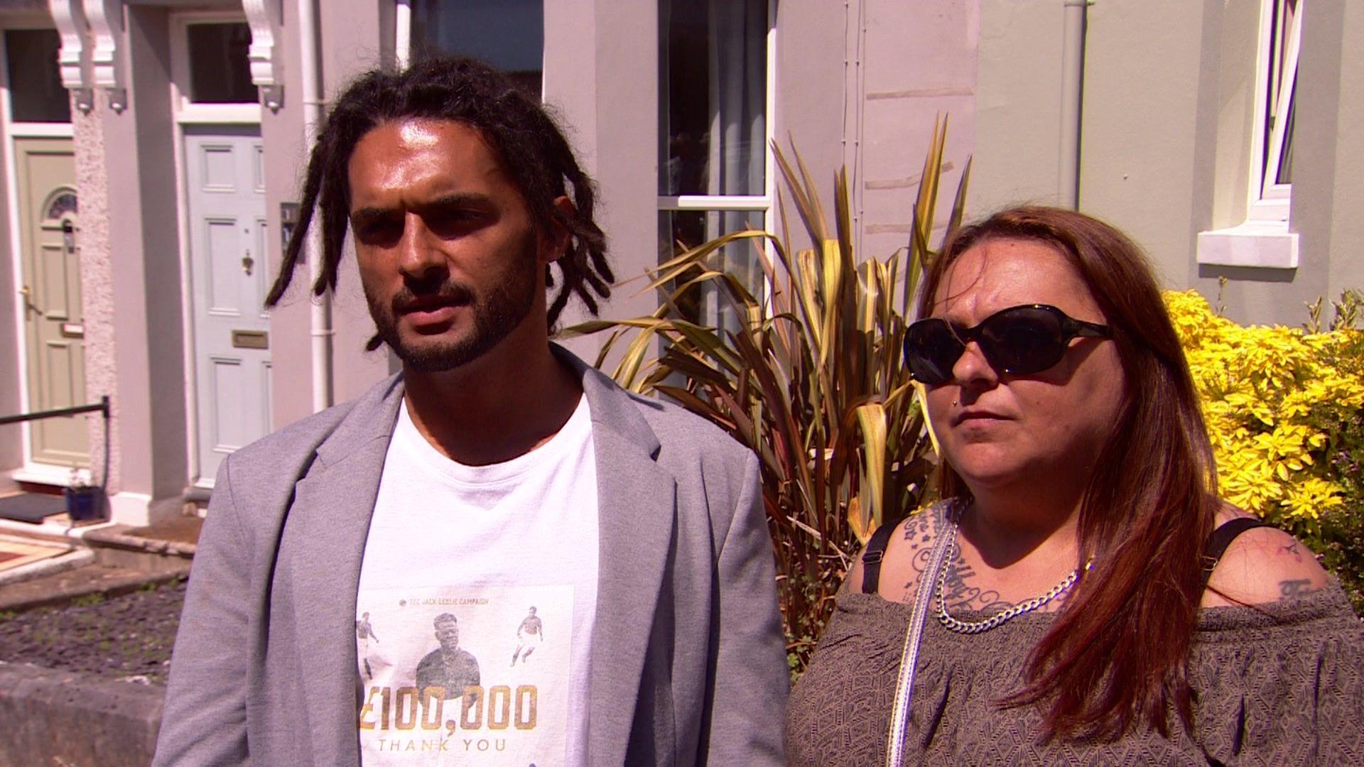 A man wearing a T shirt and light coloured jacket next to a woman with an off-the-shoulder dress and wearing dark glasses.