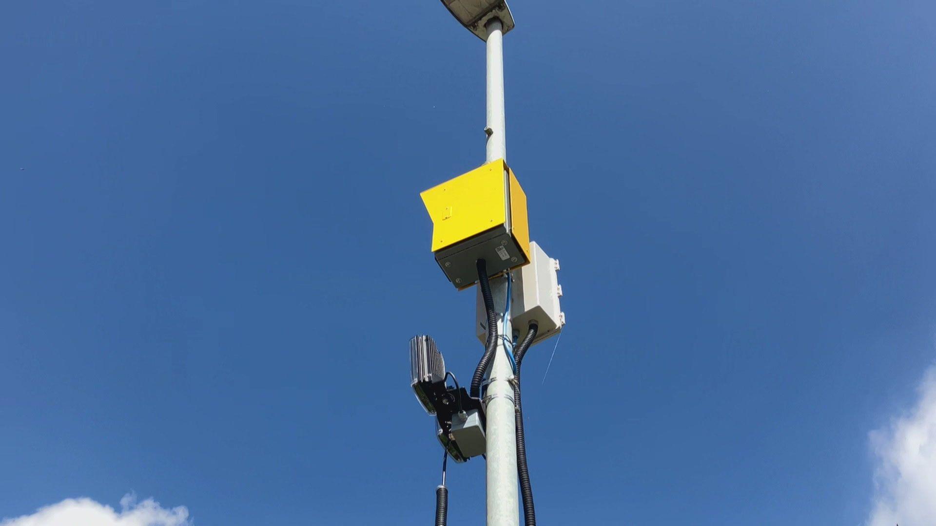 A yellow box attached to a lamp post with two sensors underneath it.