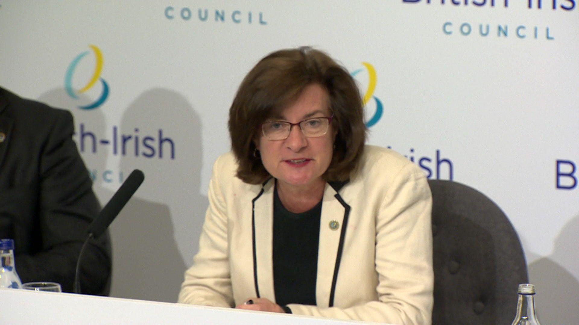 Eluned Morgan sat in a press conference with a microphone in front of her, with the British-Irish council logo on a display behind her.