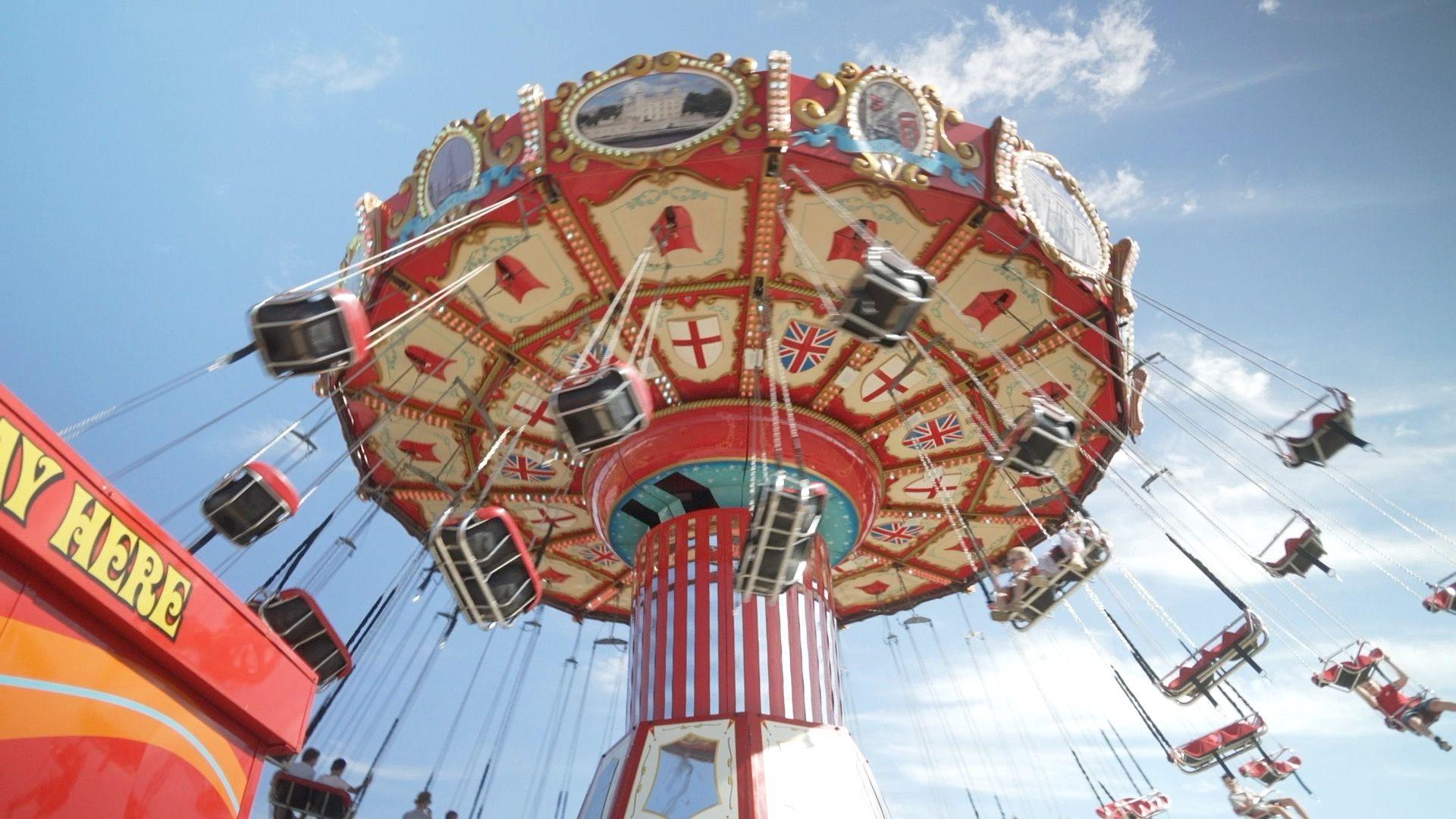 A carousel decorated in Union Jacks and St George's flag, as people swing in seats attached to the ride as it spins.  