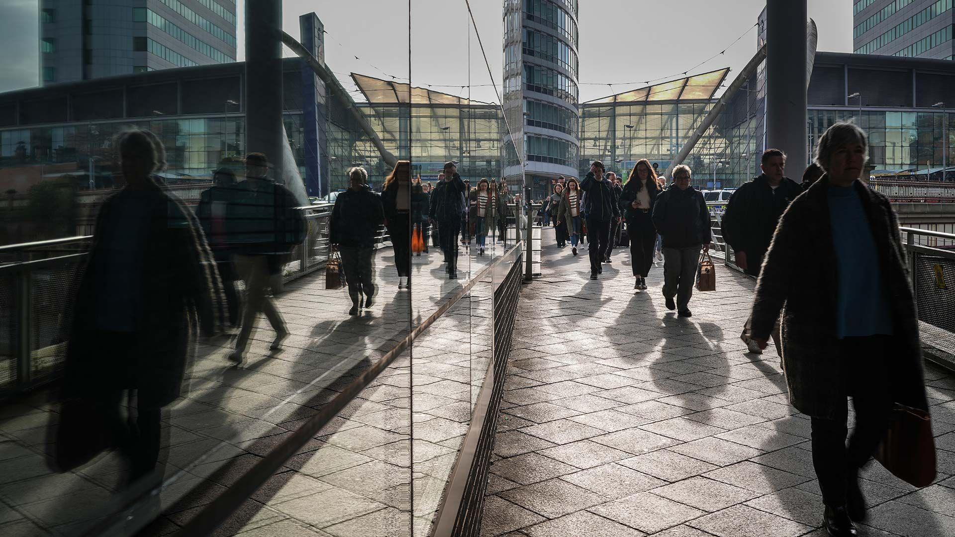 Commuters walking in shadow next to a glass building.