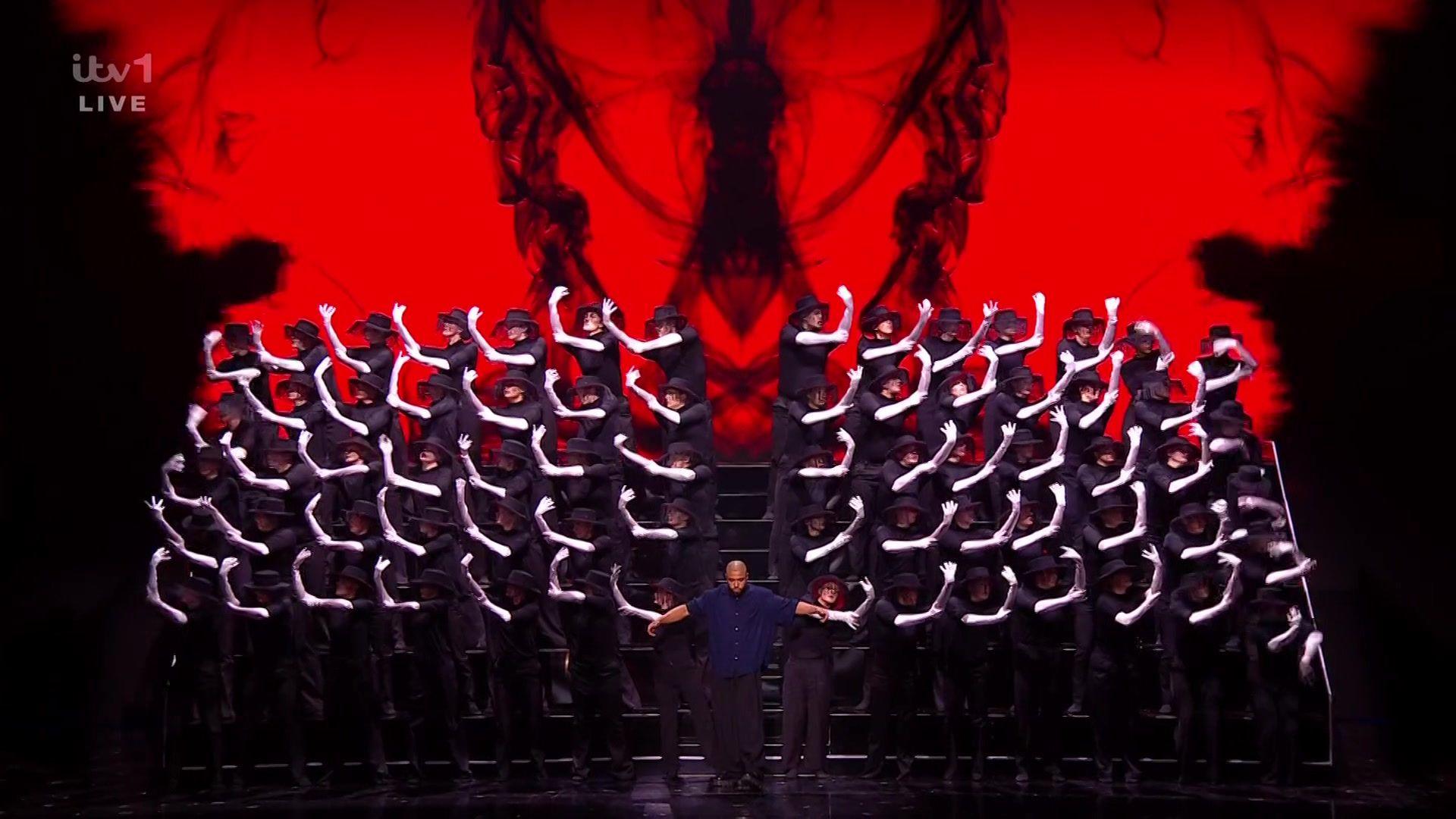 dance troupe on stage wearing black clothes and long white gloves make a striking image on a red background
