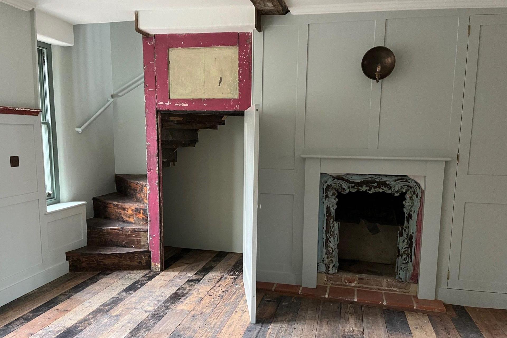 Inside the first floor of 113 Redchurch Street with a fire place in the wall and a twisting wooden staircase in the corner of the road