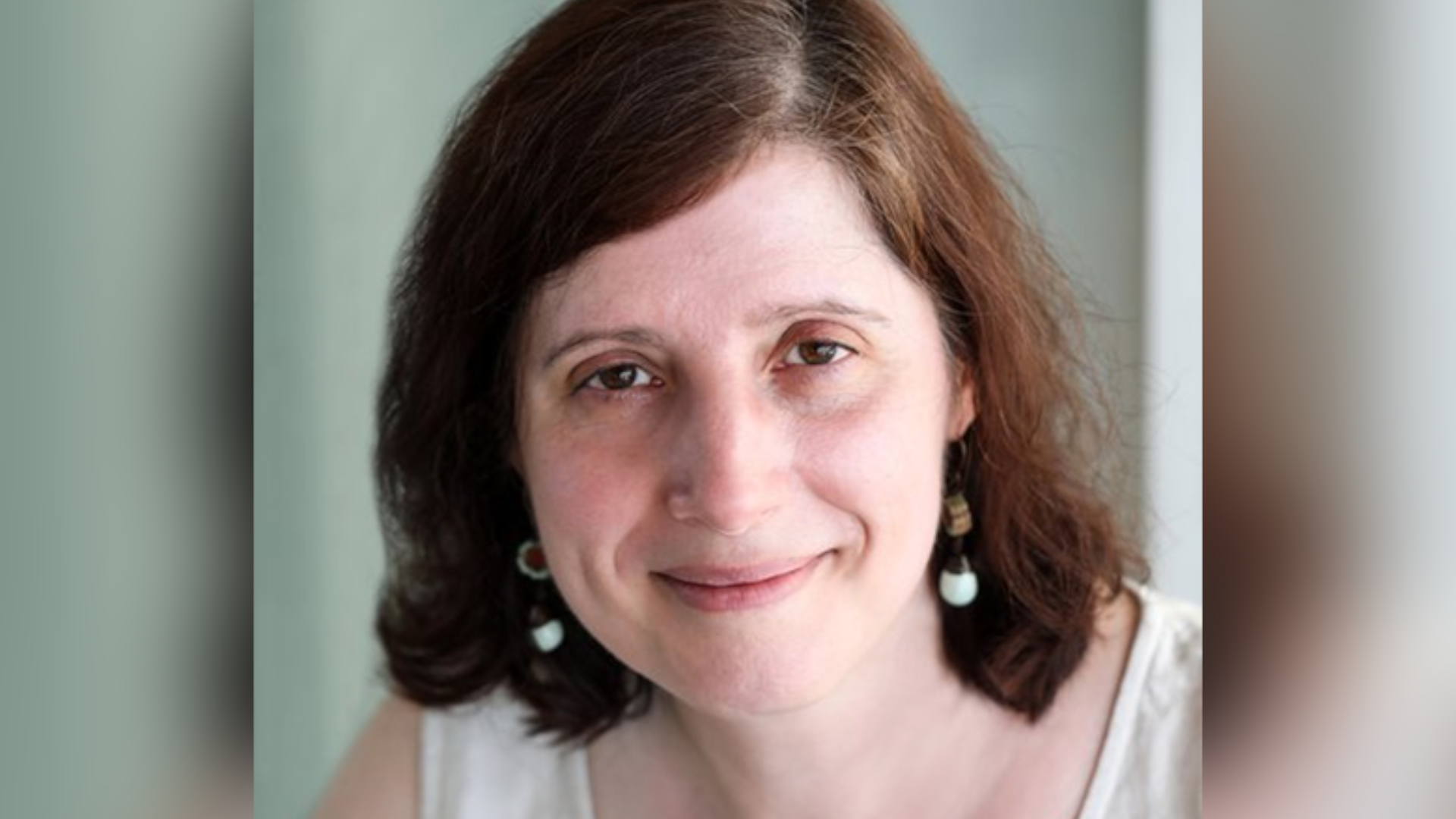 Headshot of Dr Effrossyni Gkrania-Klotsas. She is smiling while wearing a white sleeveless blouse and matching white earrings. She has shoulder length brown hair and brown eyes.