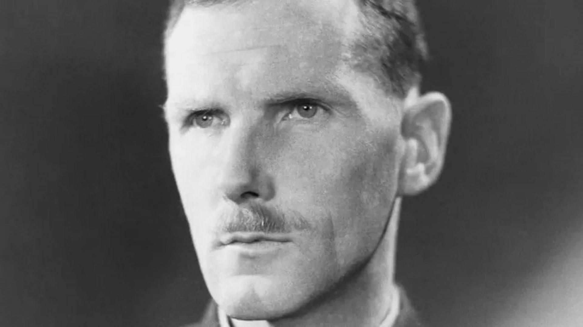 Black and white photo of moustached man, staring off camera and looking deep in thought