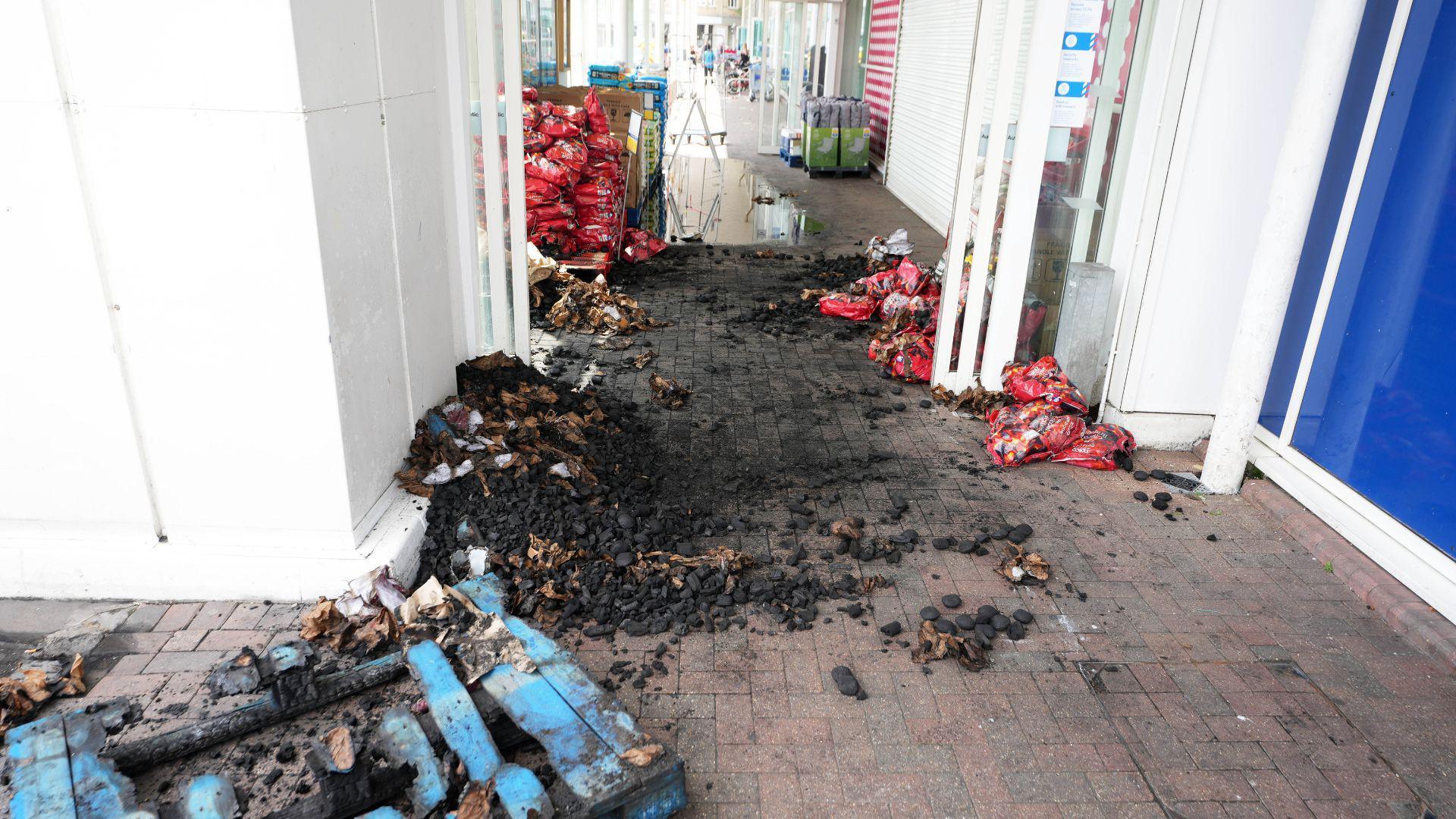 A large amount of burned charcoal and a damage blue pallet in the entrance of a supermarket