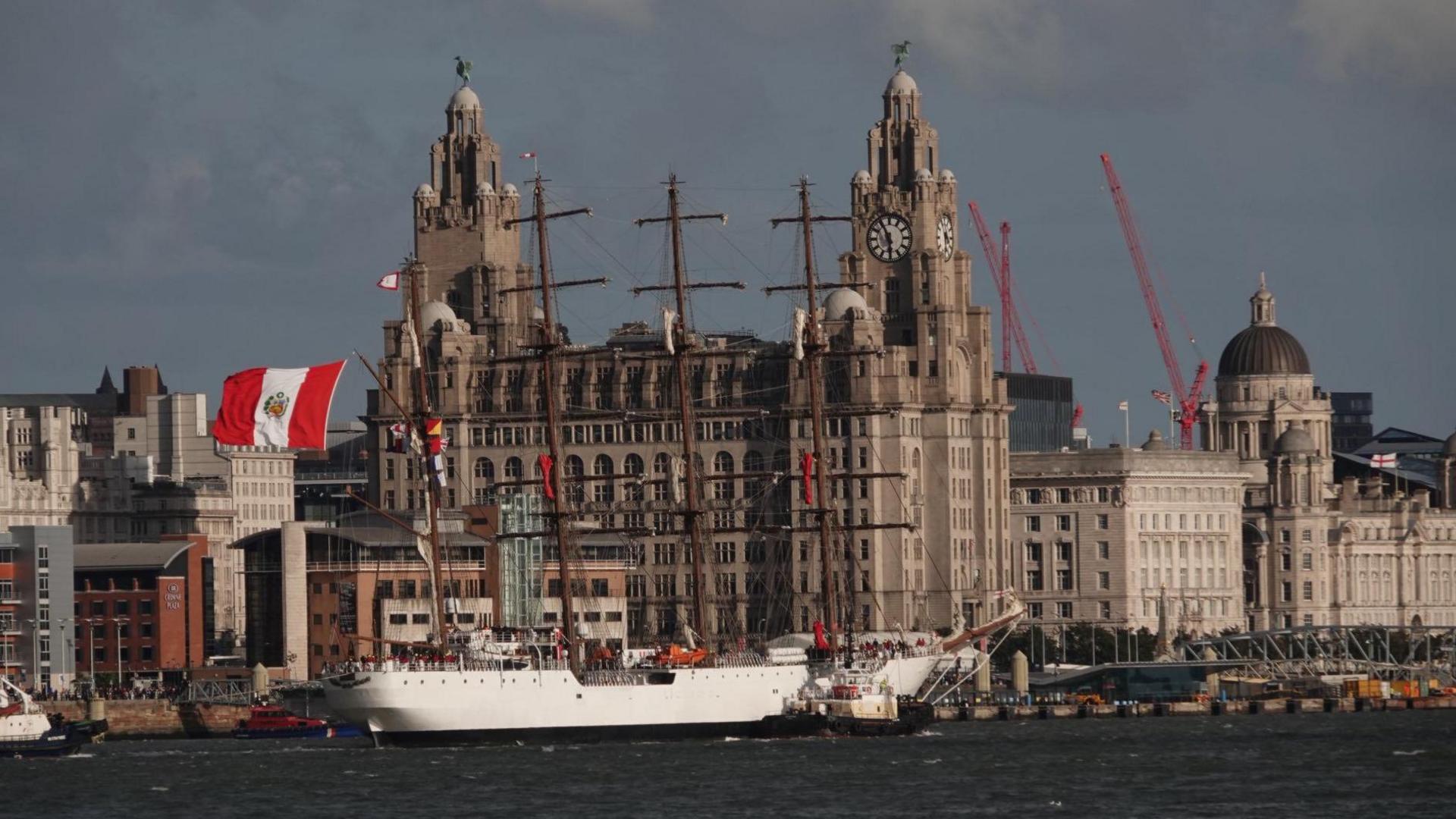 A landscape photo of the BAP Unión docked in Liverpool outside the Liver Building. The Peru flag flies on the ship's mast. 
