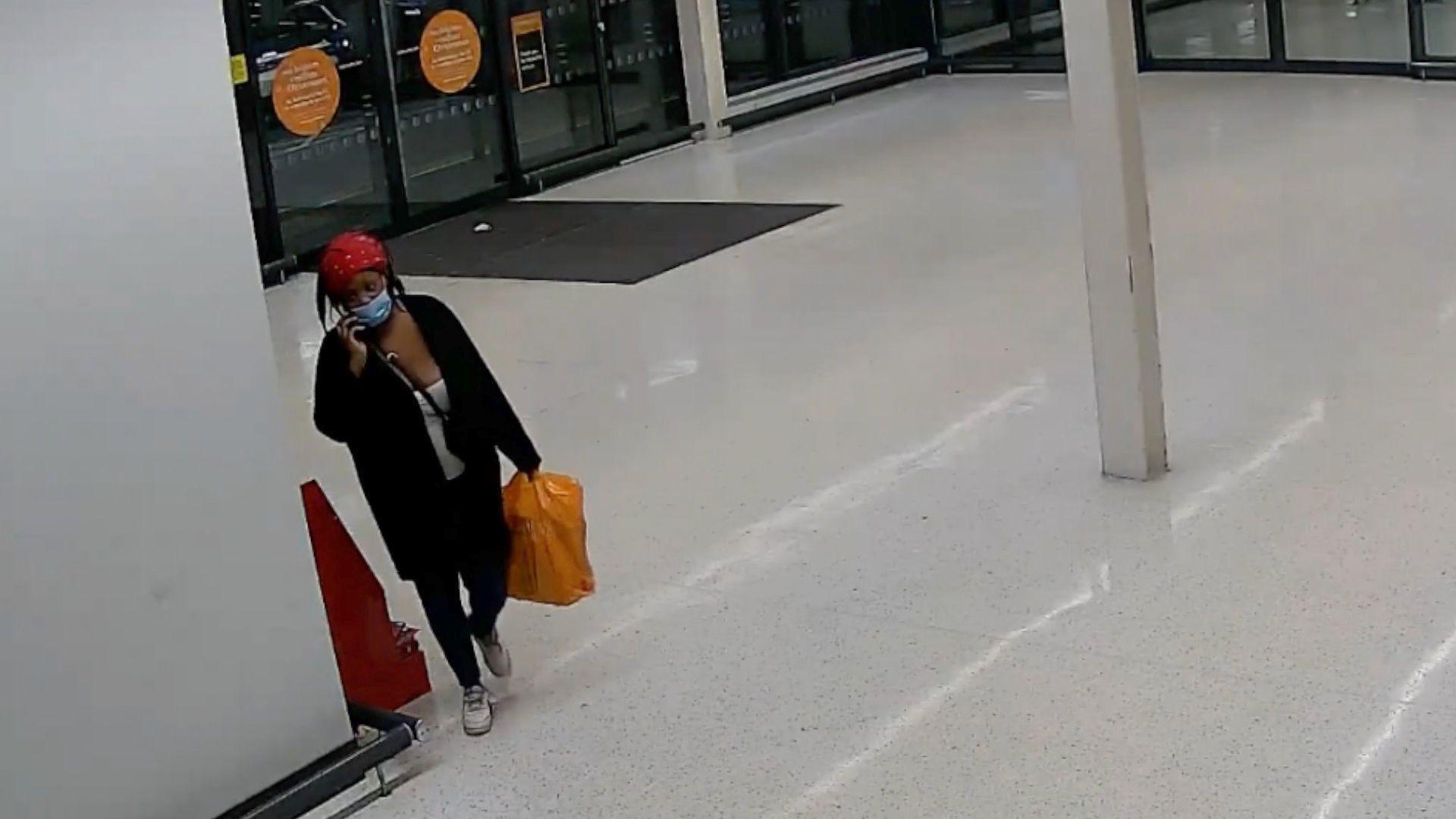 A screengrab from Metropolitan Police CCTV with Deveca Rose seen in a Sainsburys holding a large orange Sainsburys shopping bag. She is wearing a face mask and is seen with a phone by her ear. 