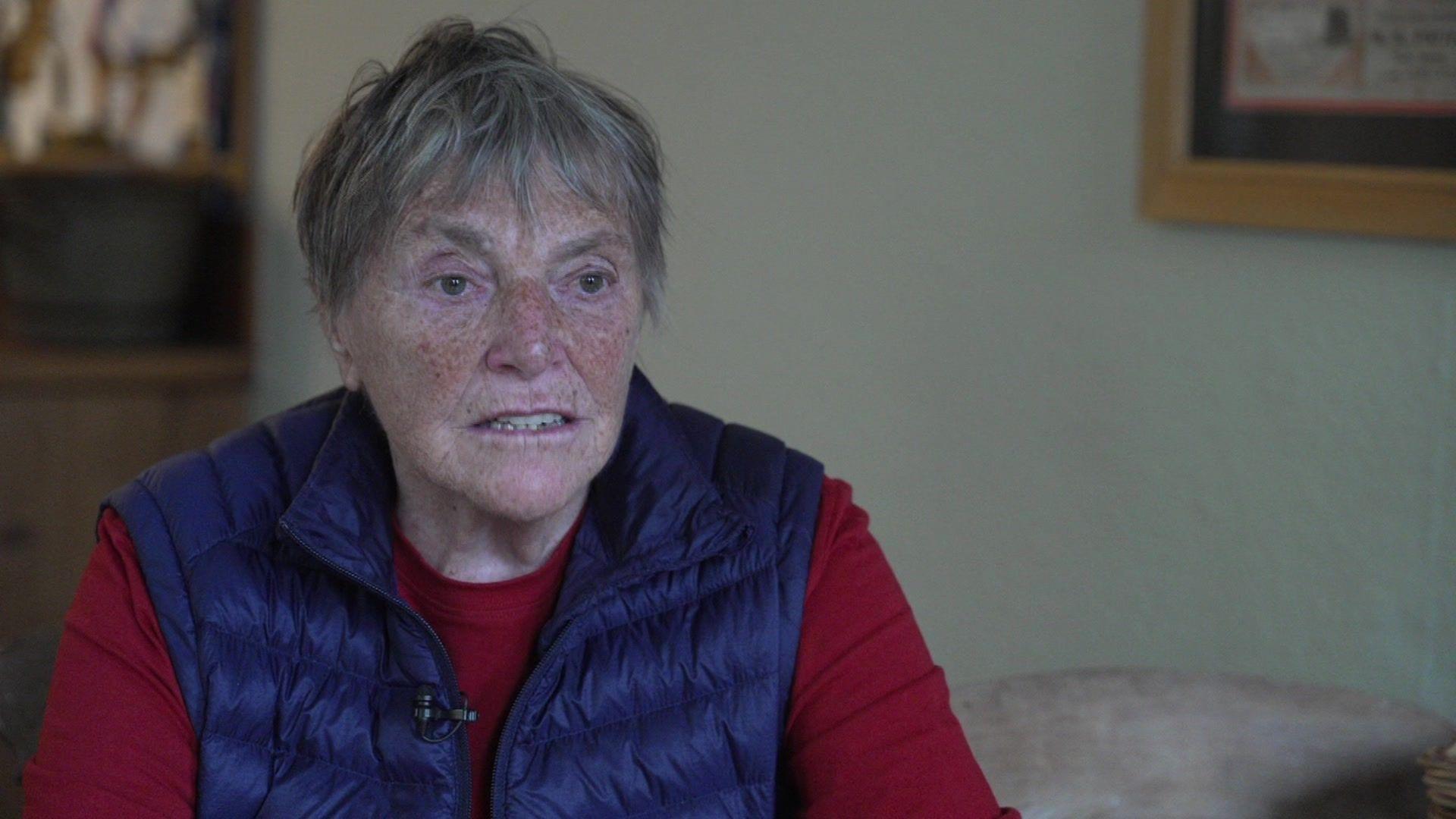 A head and shoulders image of Margaret Brotheridge who has short grey hair and is wearing a red long-sleeved top and a blue gillet